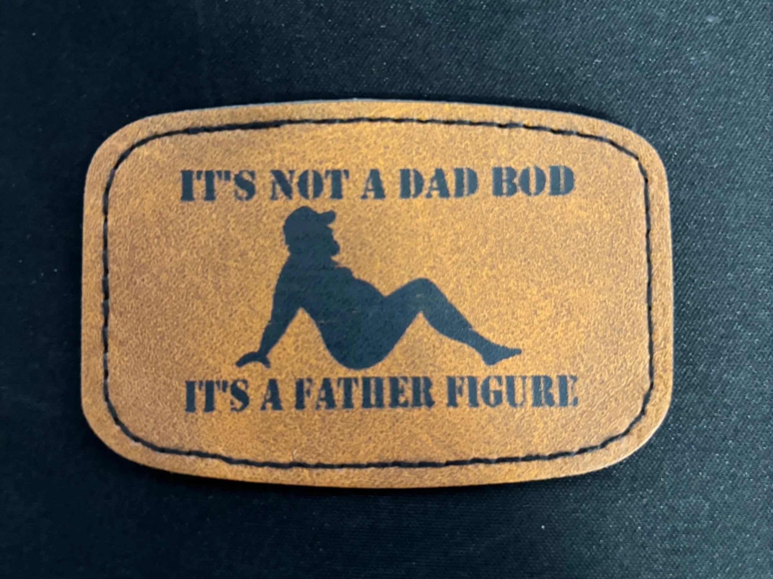 Patch with silhouette of a father figure sitting and text that reads "It's not a dad bod, it's a father figure".