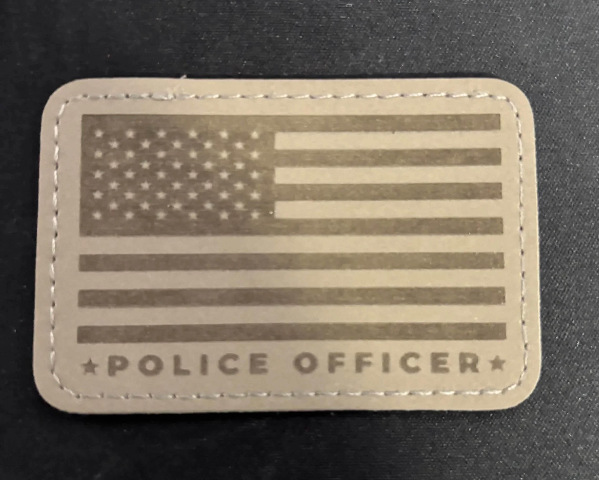 A fabric police officer badge featuring a stylized American flag design with 50 stars and 13 stripes, and the words 'POLICE OFFICER' at the bottom.