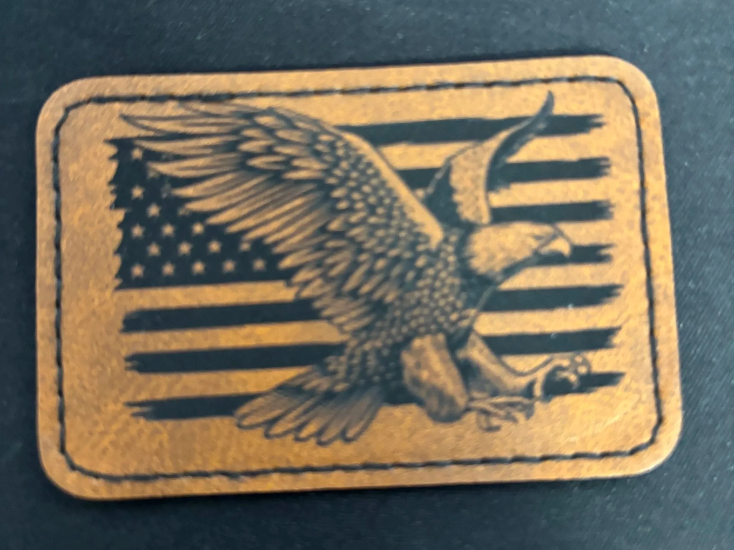 Leather patch with a design of an American flag and a bald eagle in front of it.