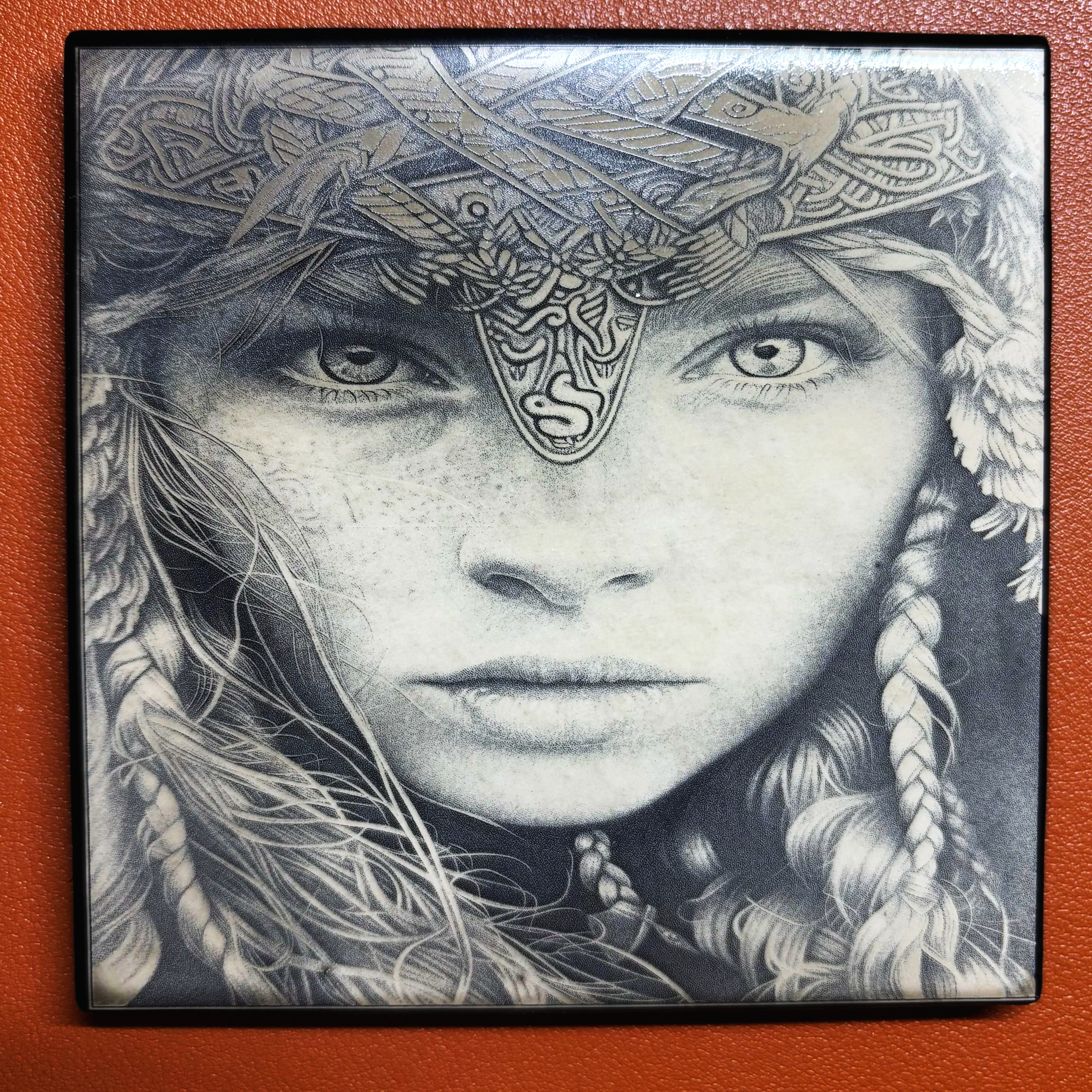 A black and white portrait of a woman with detailed braided hair, wearing a headdress with intricate patterns and symbols