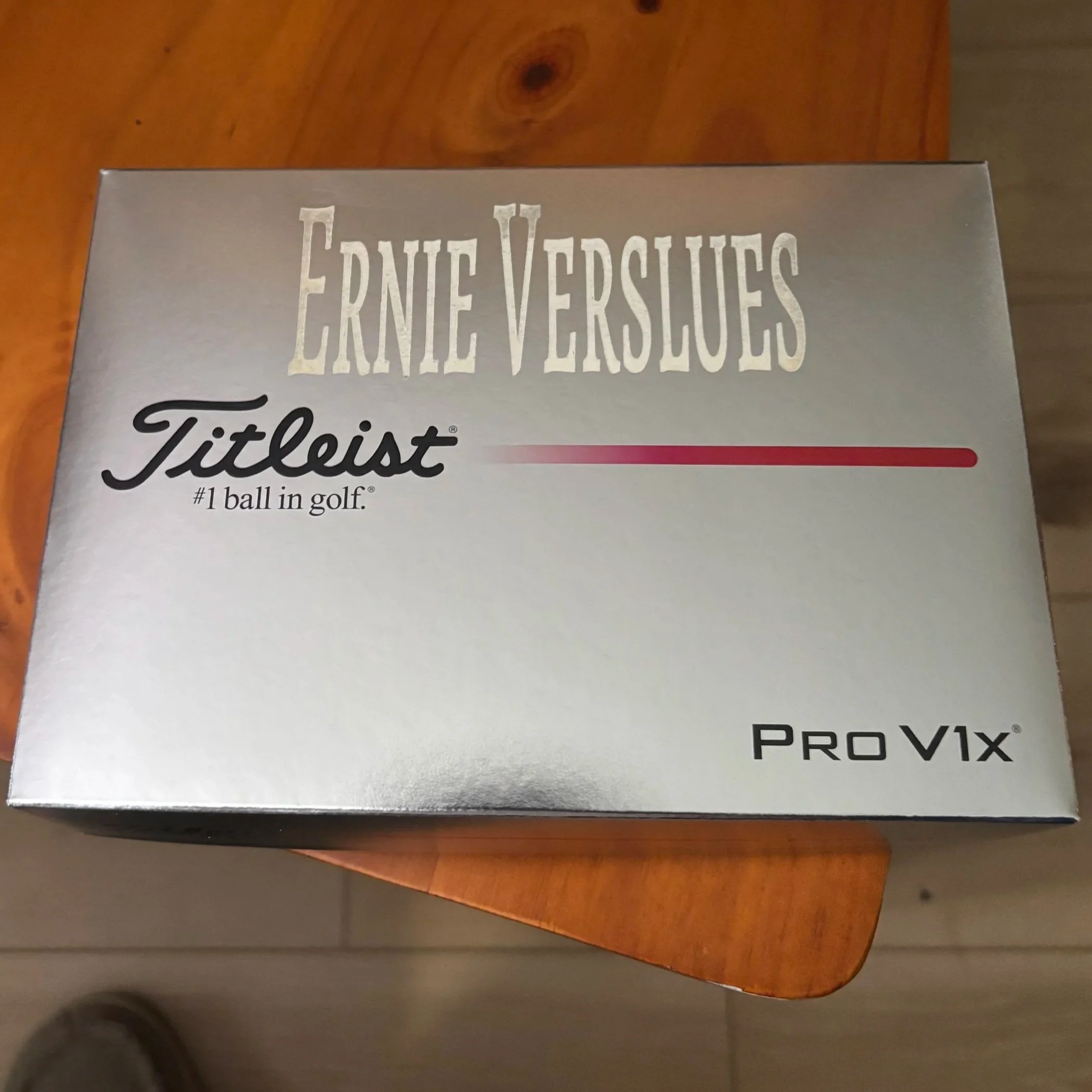 Silver box of Ernie Versluis Titleist golf balls, model Pro V1x, placed on a wooden table.