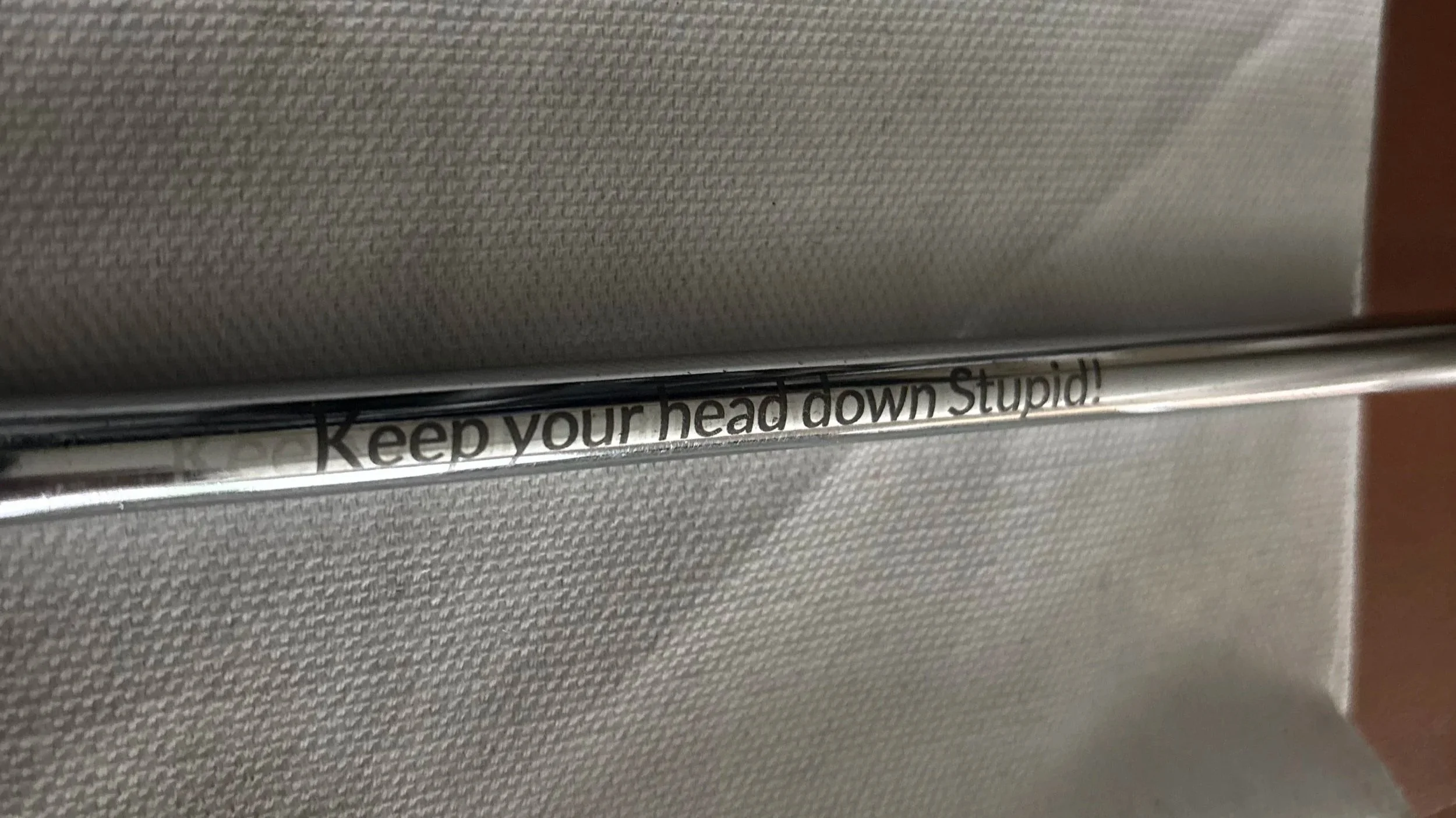 A reflective metallic surface with a sticker that has the partial text, 'Keep your head down Stupid!'