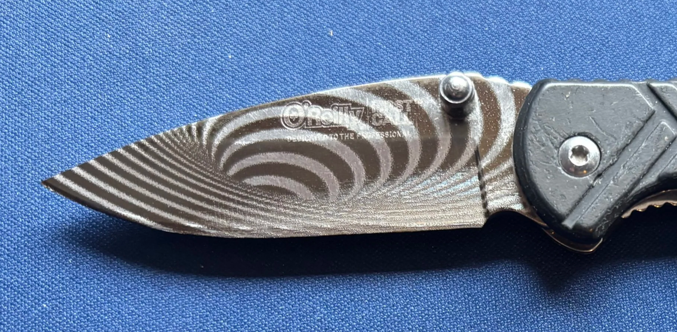 A folding pocket knife with a black handle and a textured grip, partially open to reveal a patterned silver blade with a swirling design.