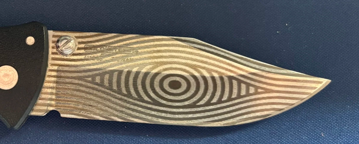 A folding pocket knife with a black handle and a patterned metallic blade.