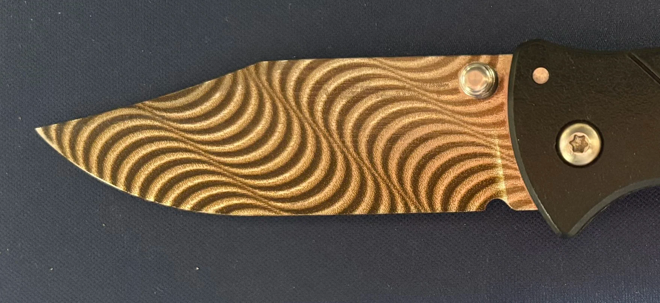 A folding pocket knife with a patterned gold and black handle on a dark blue surface.