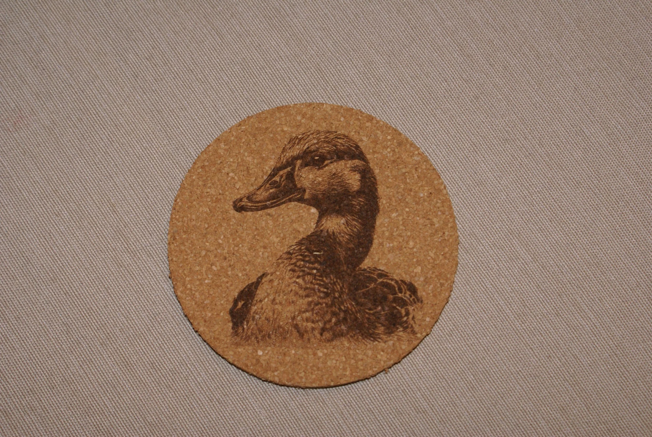 Round cork coaster with vintage-style illustration of a duck's head and neck.