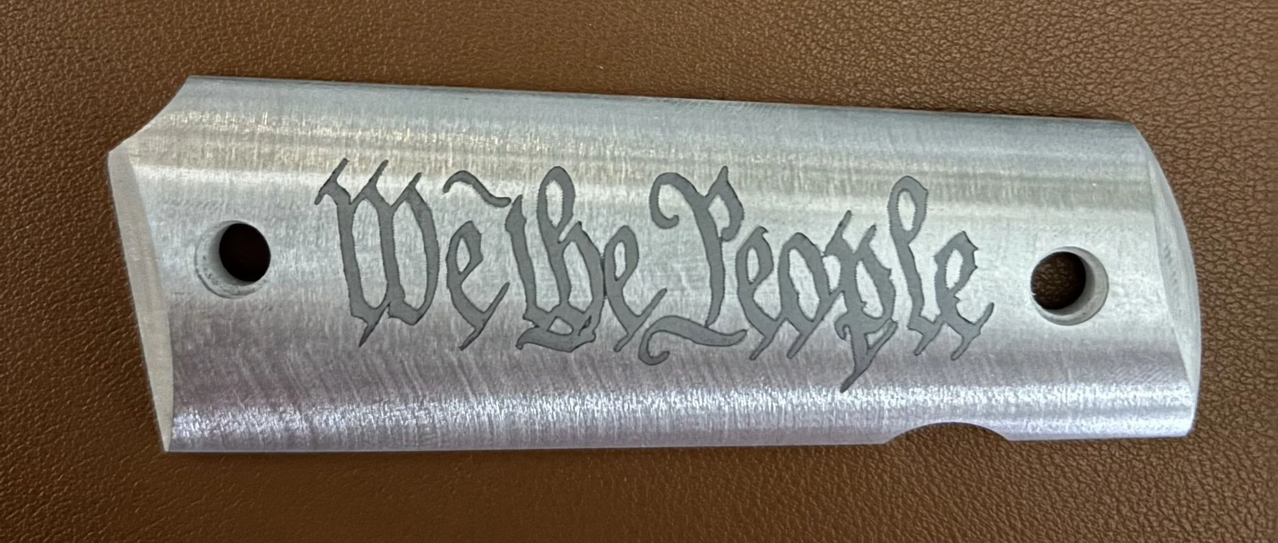 A metallic safety razor blade with the words "We the People" engraved on it.