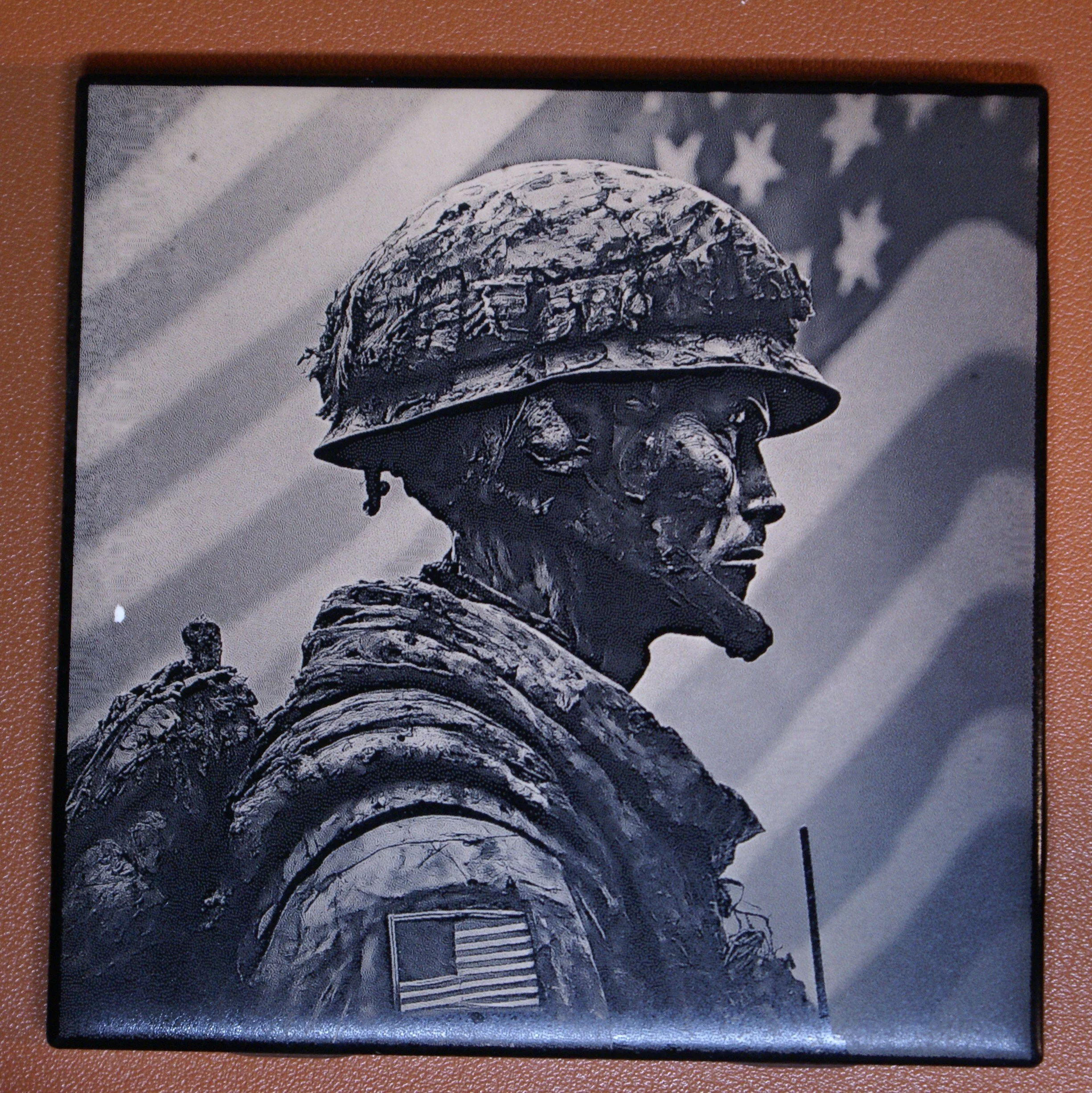 A black and white sculpture of a soldier in profile view wearing a helmet, with an American flag in the background.