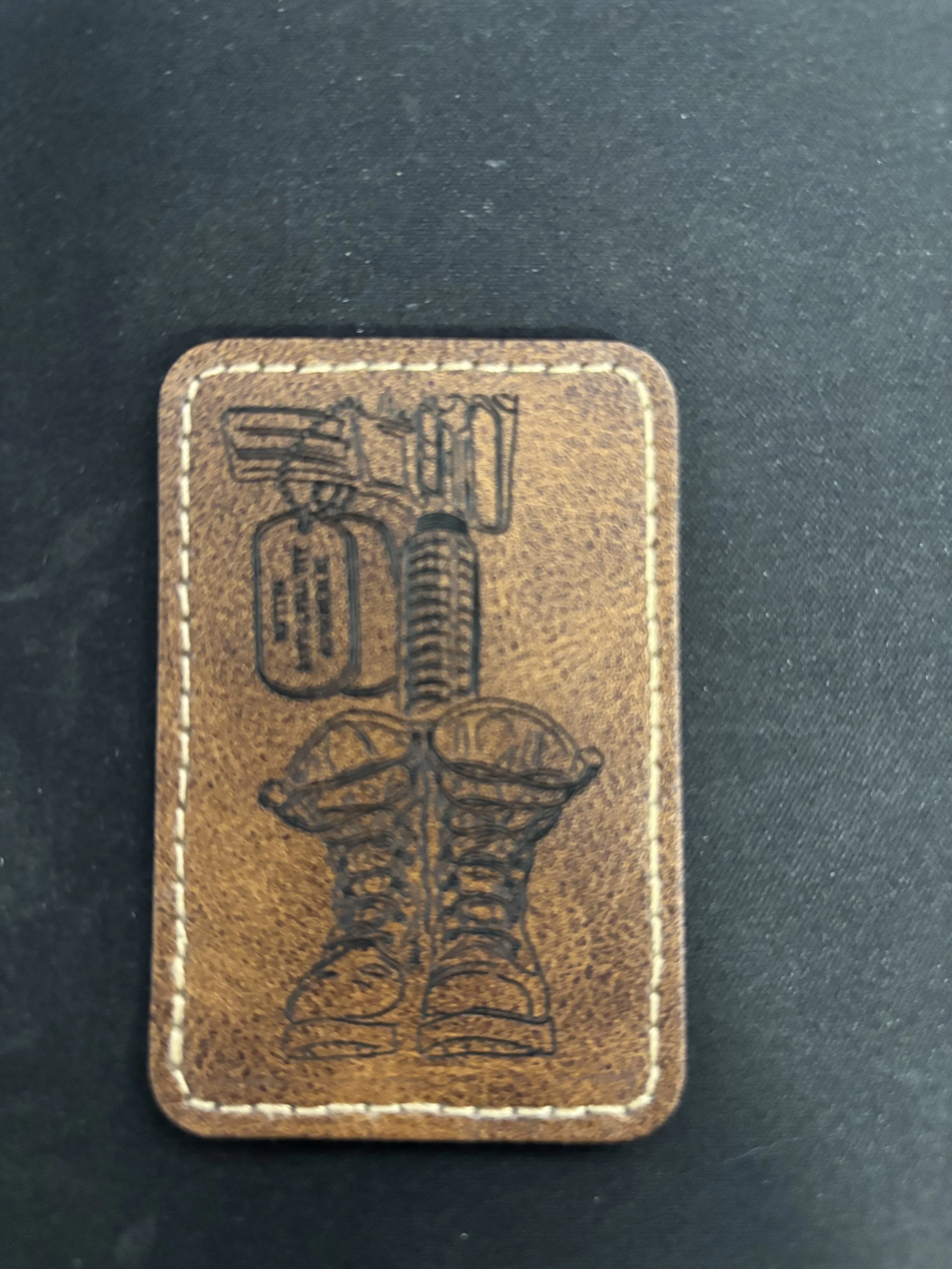 A leather patch with an illustration of military boots, a grenade, and a tactical vest with magazines.