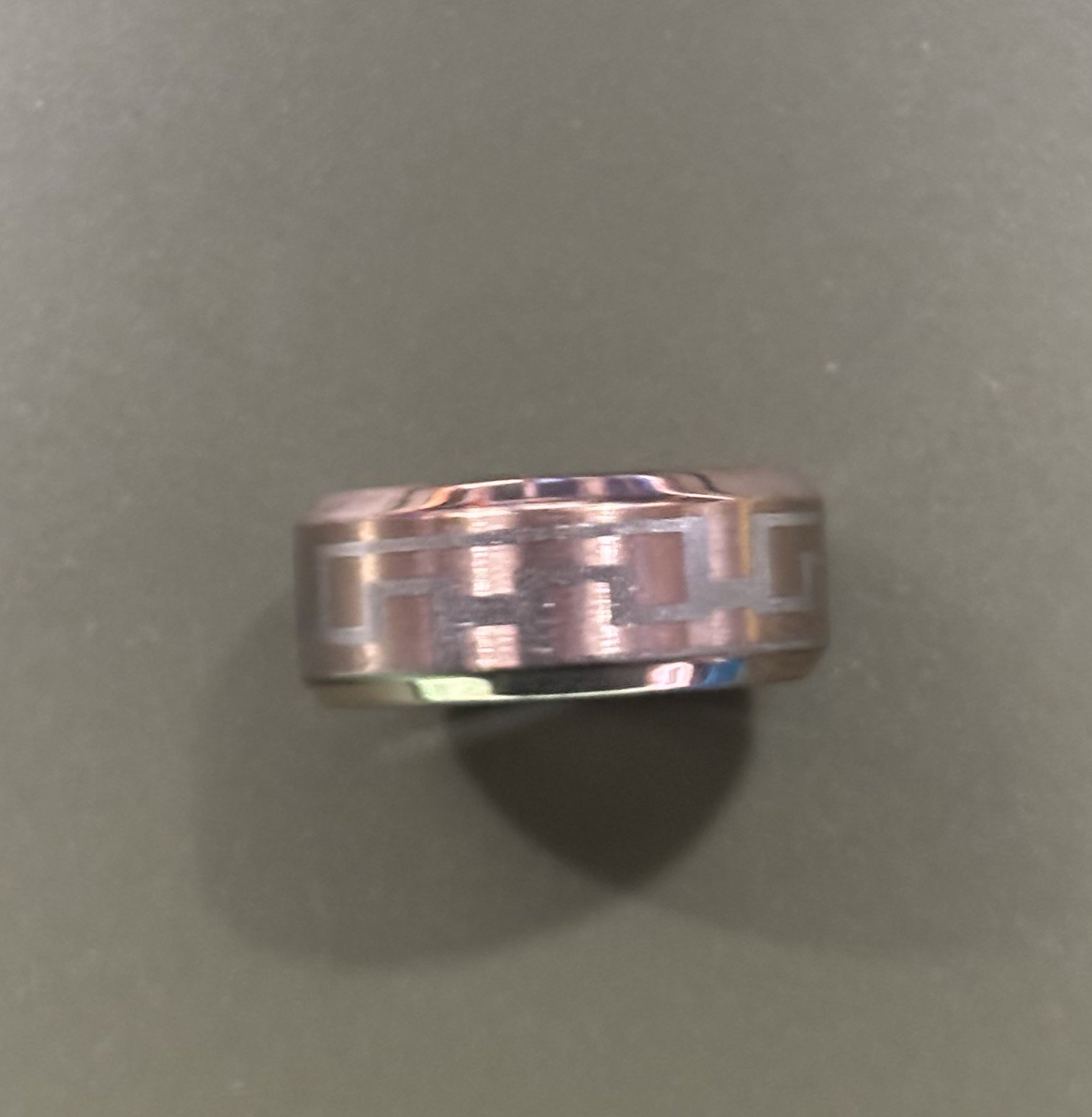 A silver ring with engraved geometric pattern on a gray background.