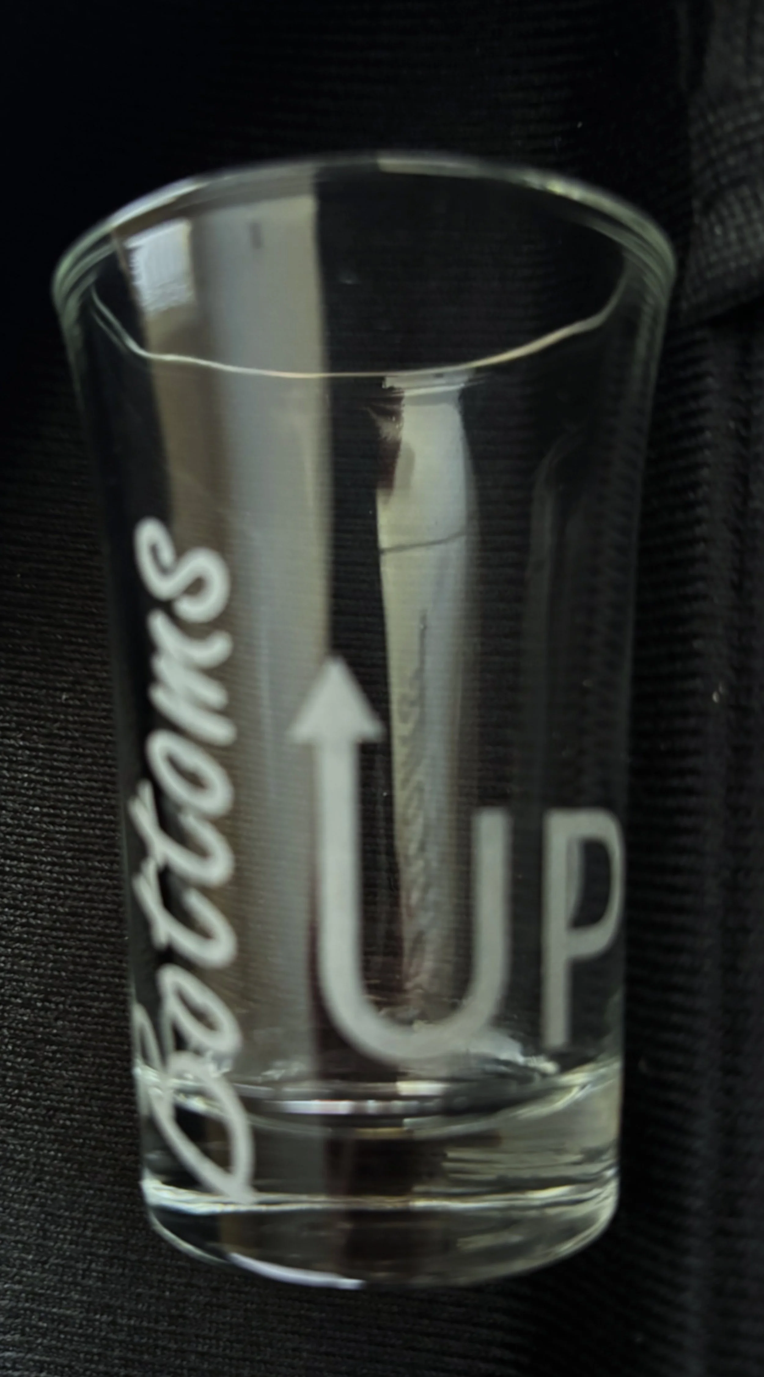 Clear glass with printed white graphics of a U-shaped arrow pointed upward, the word 'up,' and the word 'bottoms' partially visible.