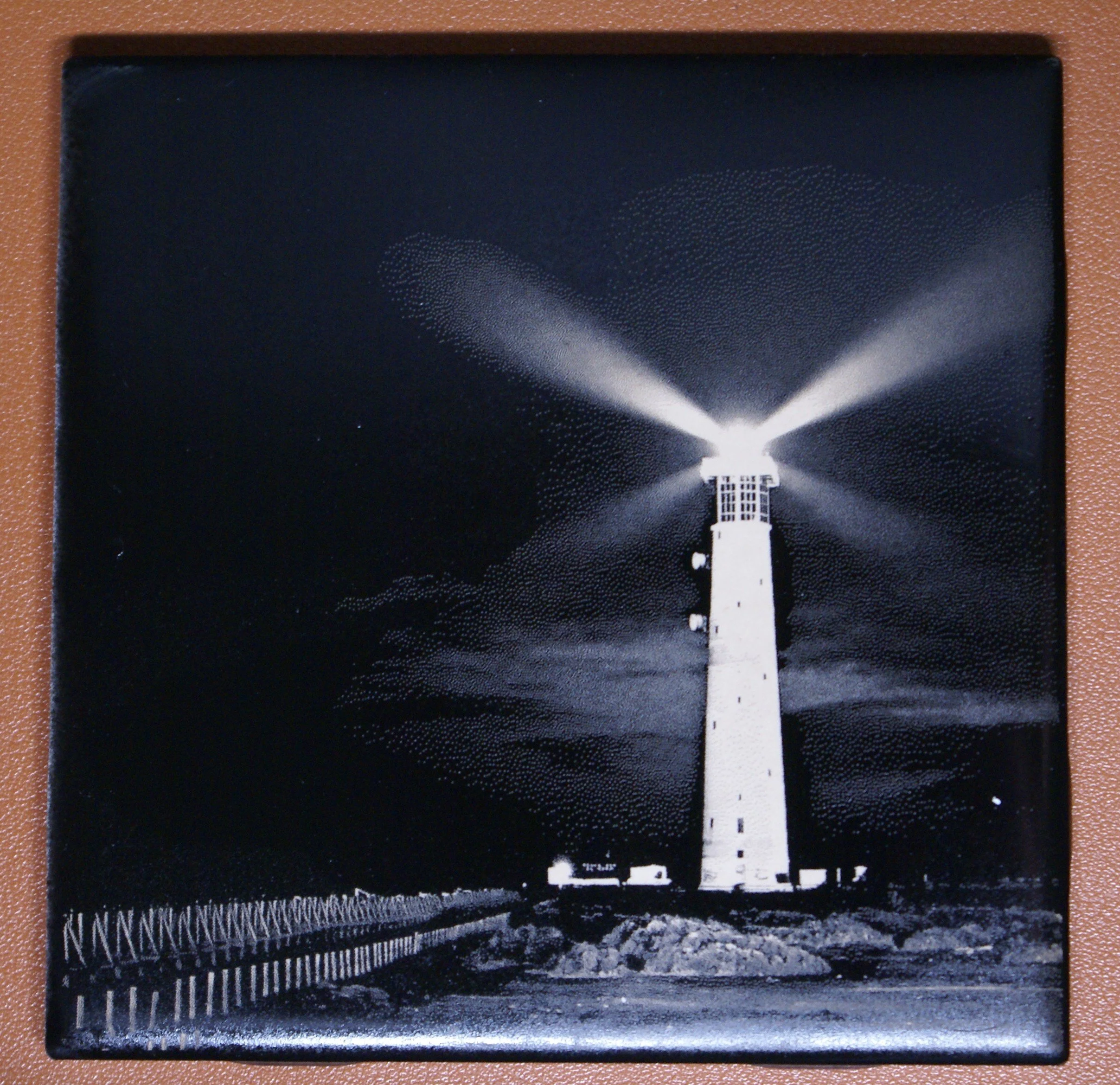 Black-and-white photo of a lighthouse with bright beams of light splashing out in multiple directions at night.