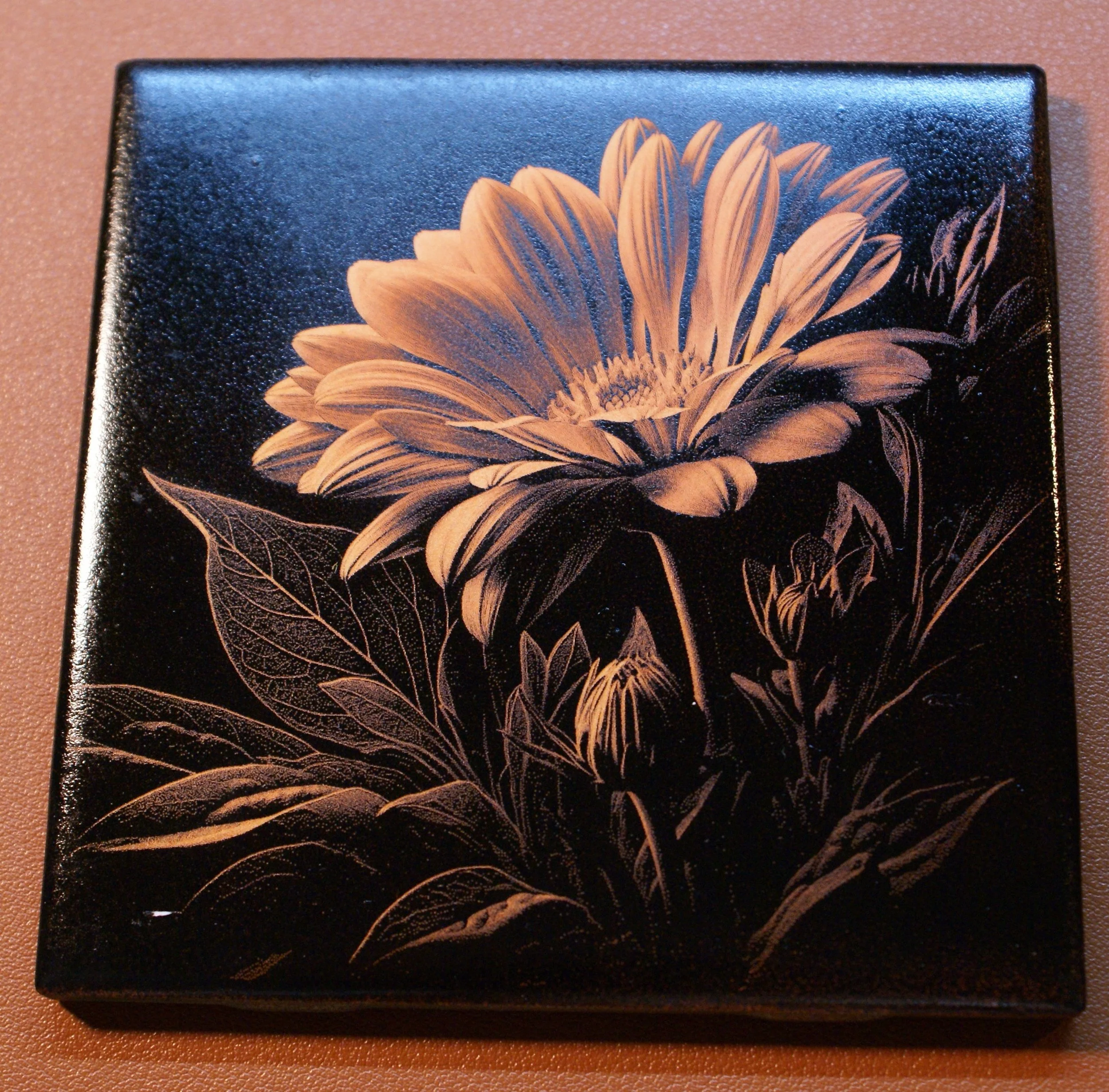 A black box decorated with a detailed gold floral design of a large flower with leaves and smaller flowers.