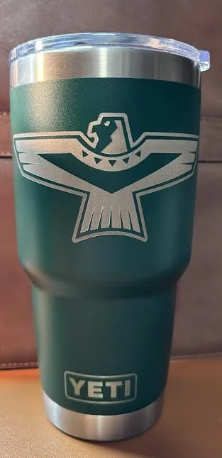 A green YETI tumbler with a silver lid, featuring a logo of an eagle with outstretched wings and a tag on its neck.