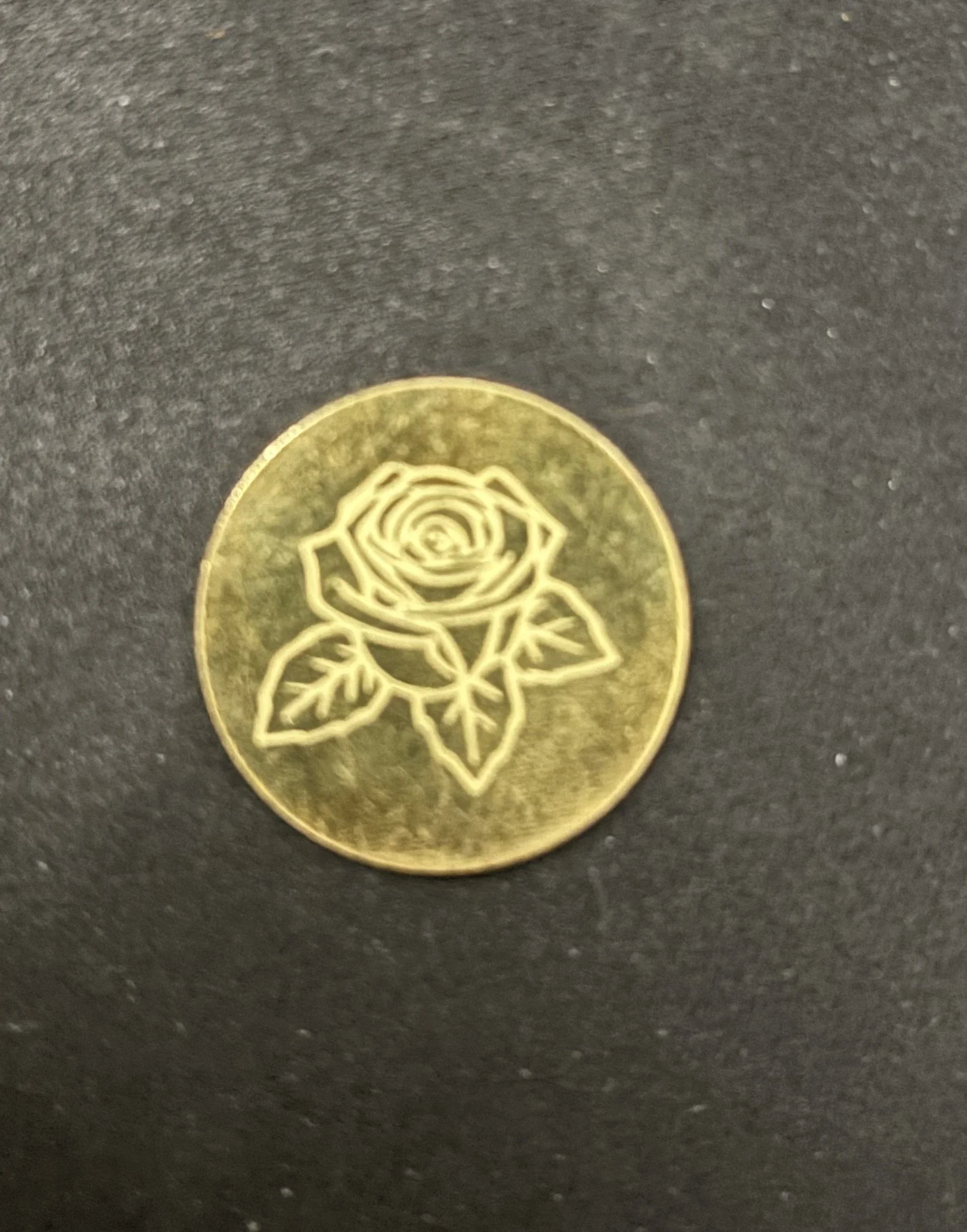 A gold coin with a line art of a rose and leaves engraved on it.