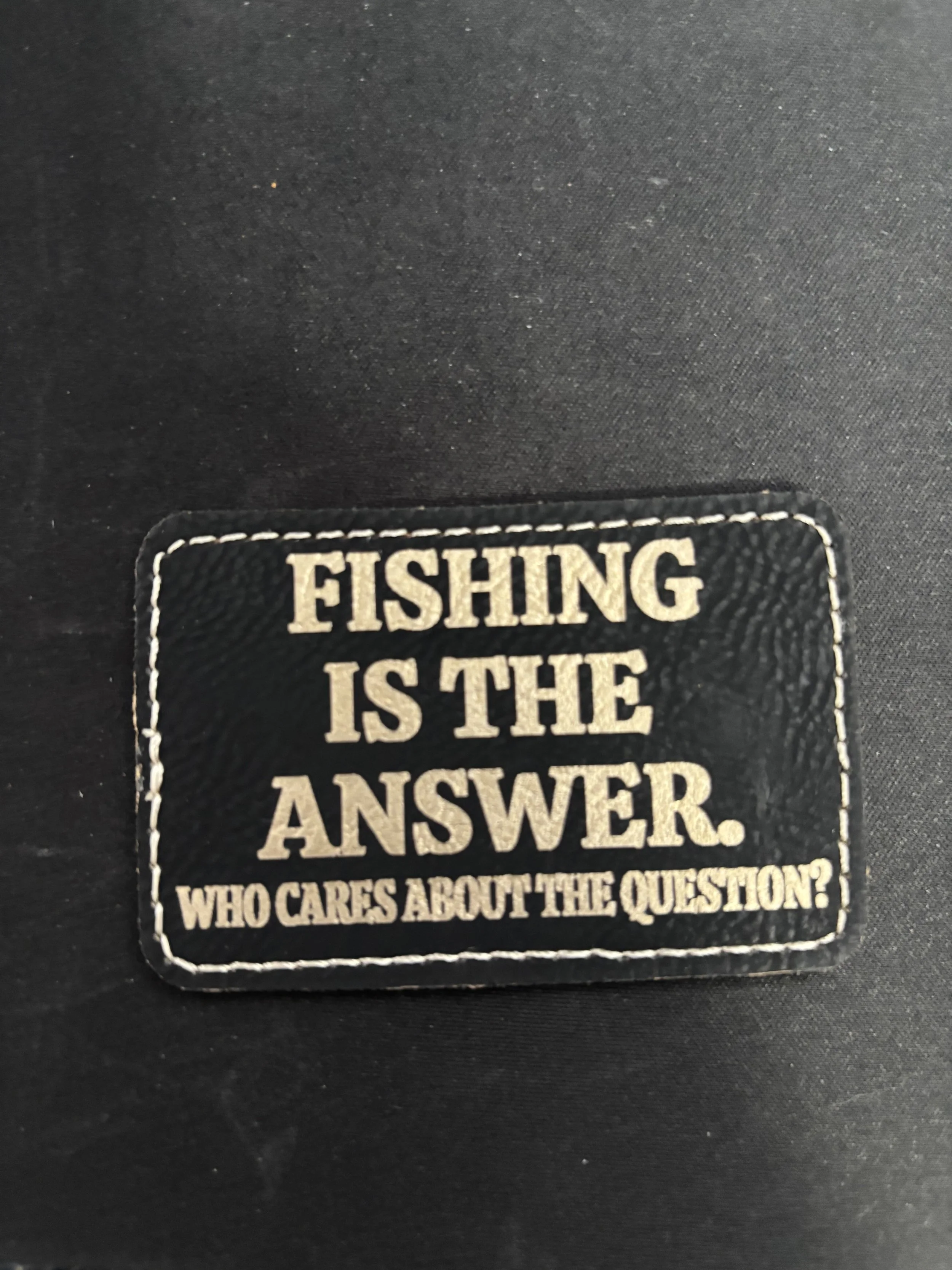 Patch with the text 'FISHING IS THE ANSWER. WHO CARES ABOUT THE QUESTION?' sewn onto dark fabric.