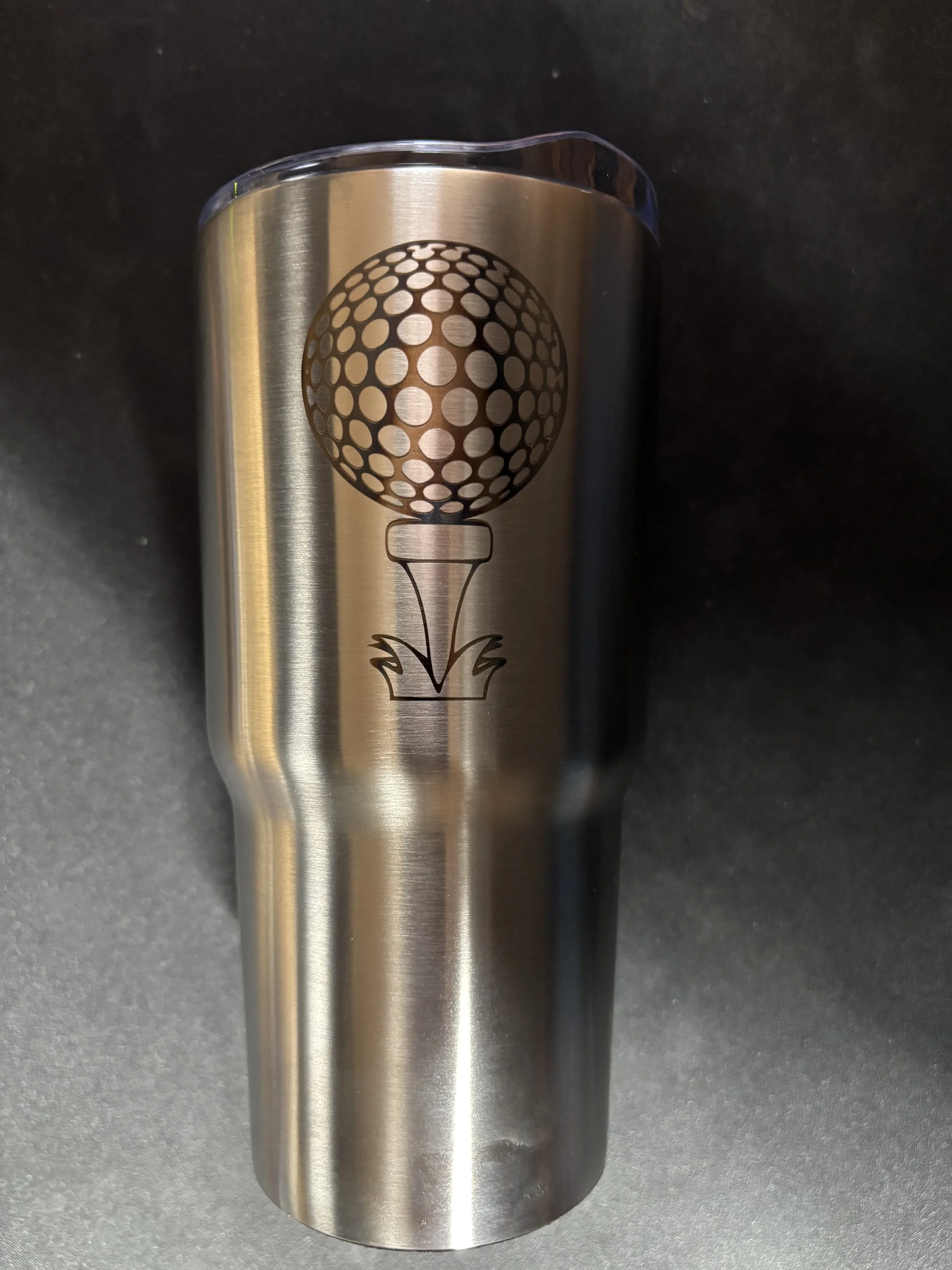 A stainless steel tumbler with a black golf ball graphic and tee illustration on it.