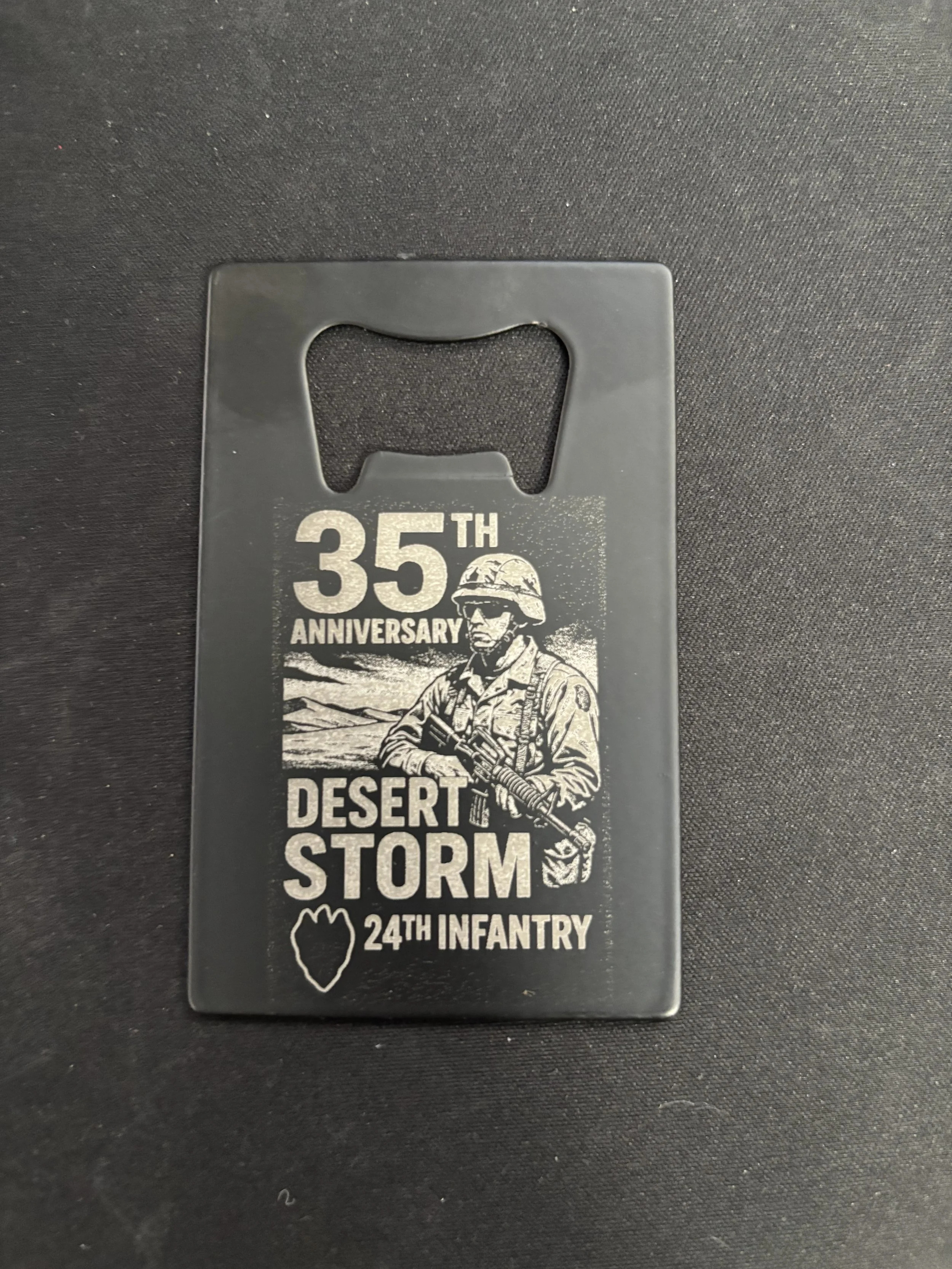 Black commemorative bottle opener with engraved text and image celebrating the 35th anniversary of Desert Storm, featuring a soldier illustration and a small outlined map of Iraq.