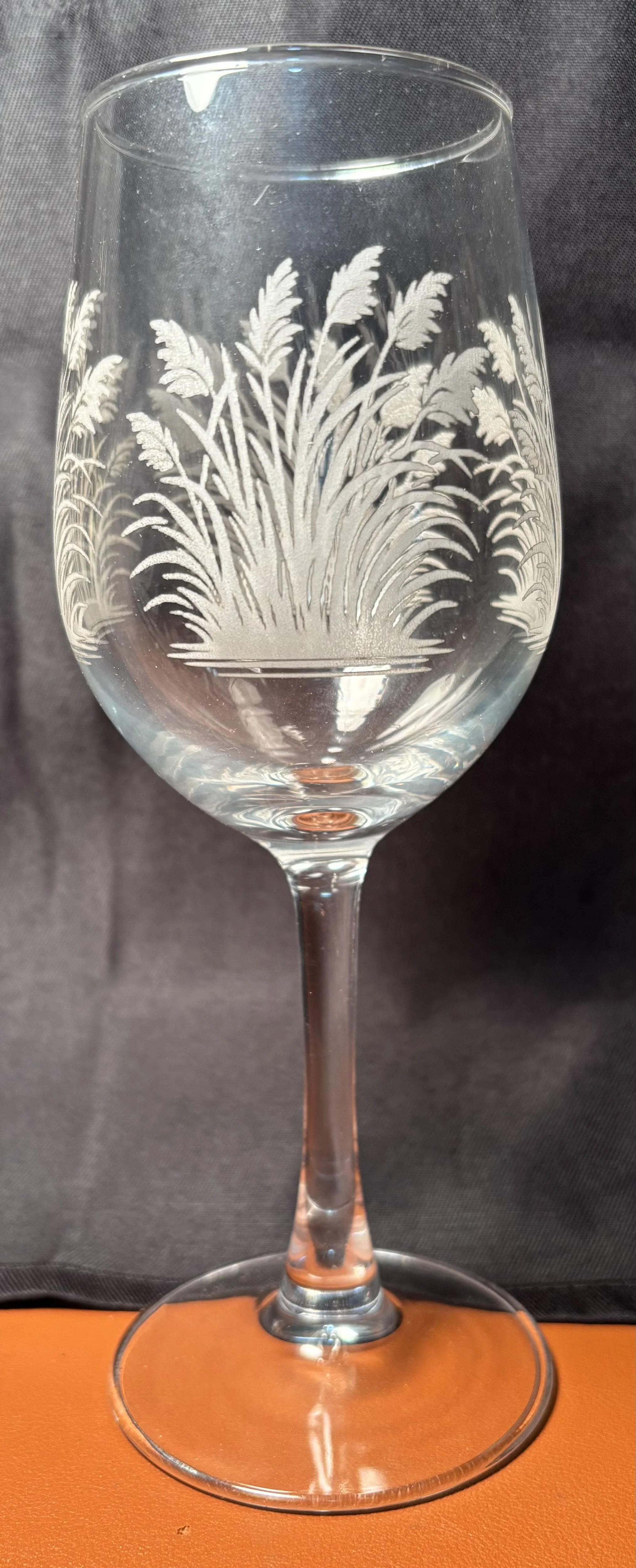 A clear glass with unwanted etched design of a plant or grass on the bowl of the glass.