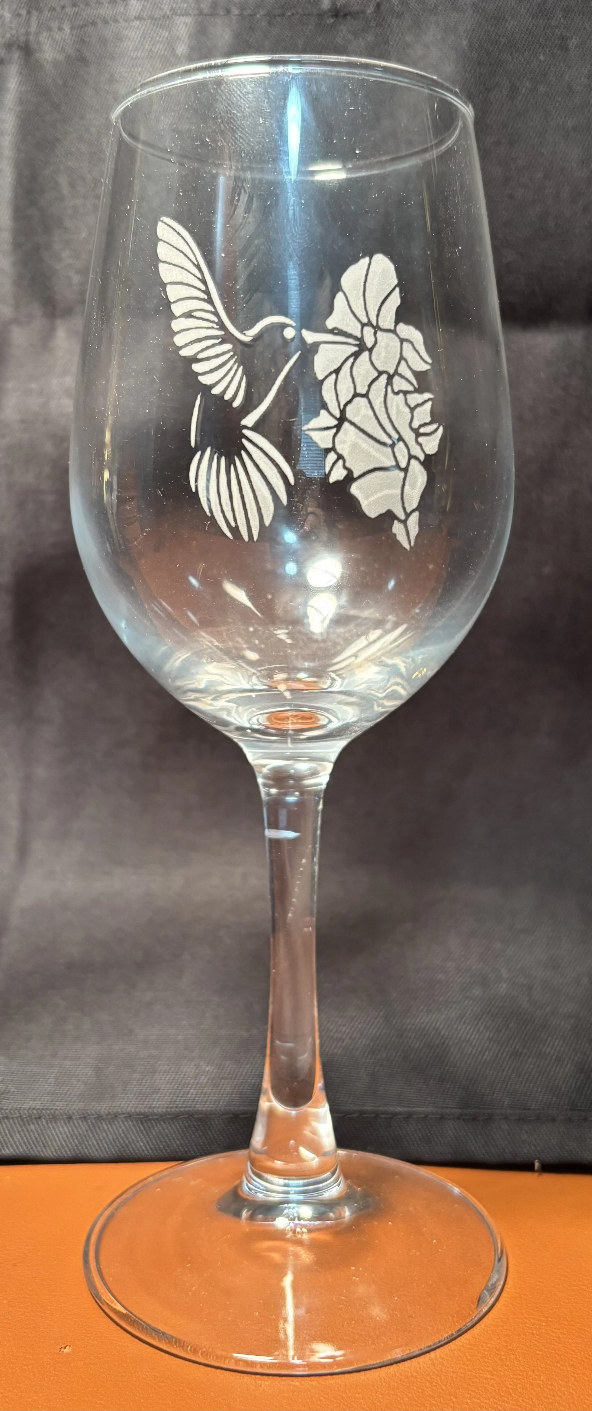 A clear wine glass with etched design of a hummingbird and flowers.