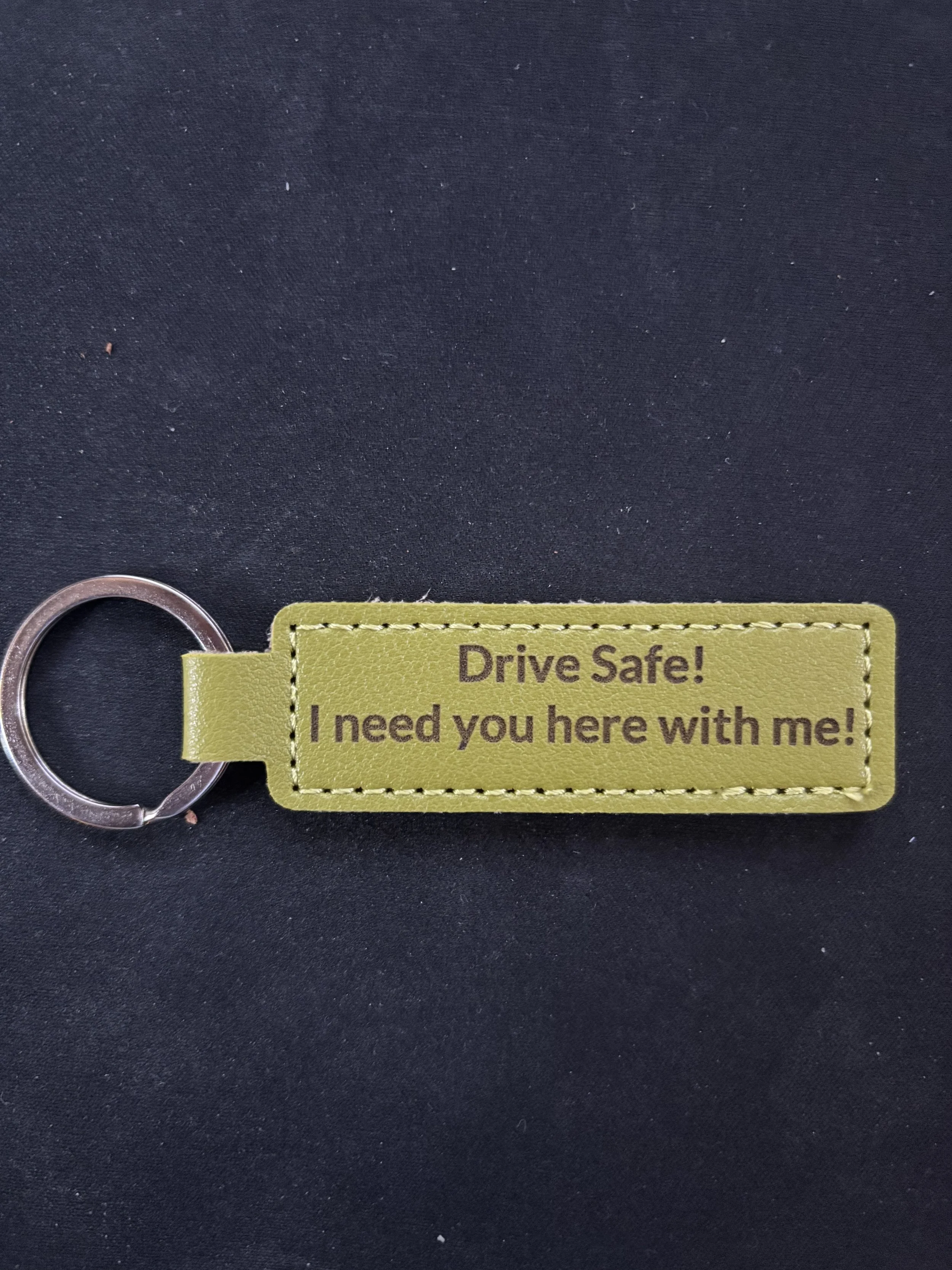 Green keychain with text: "Drive Safe! I need you here with me!" on a black background.