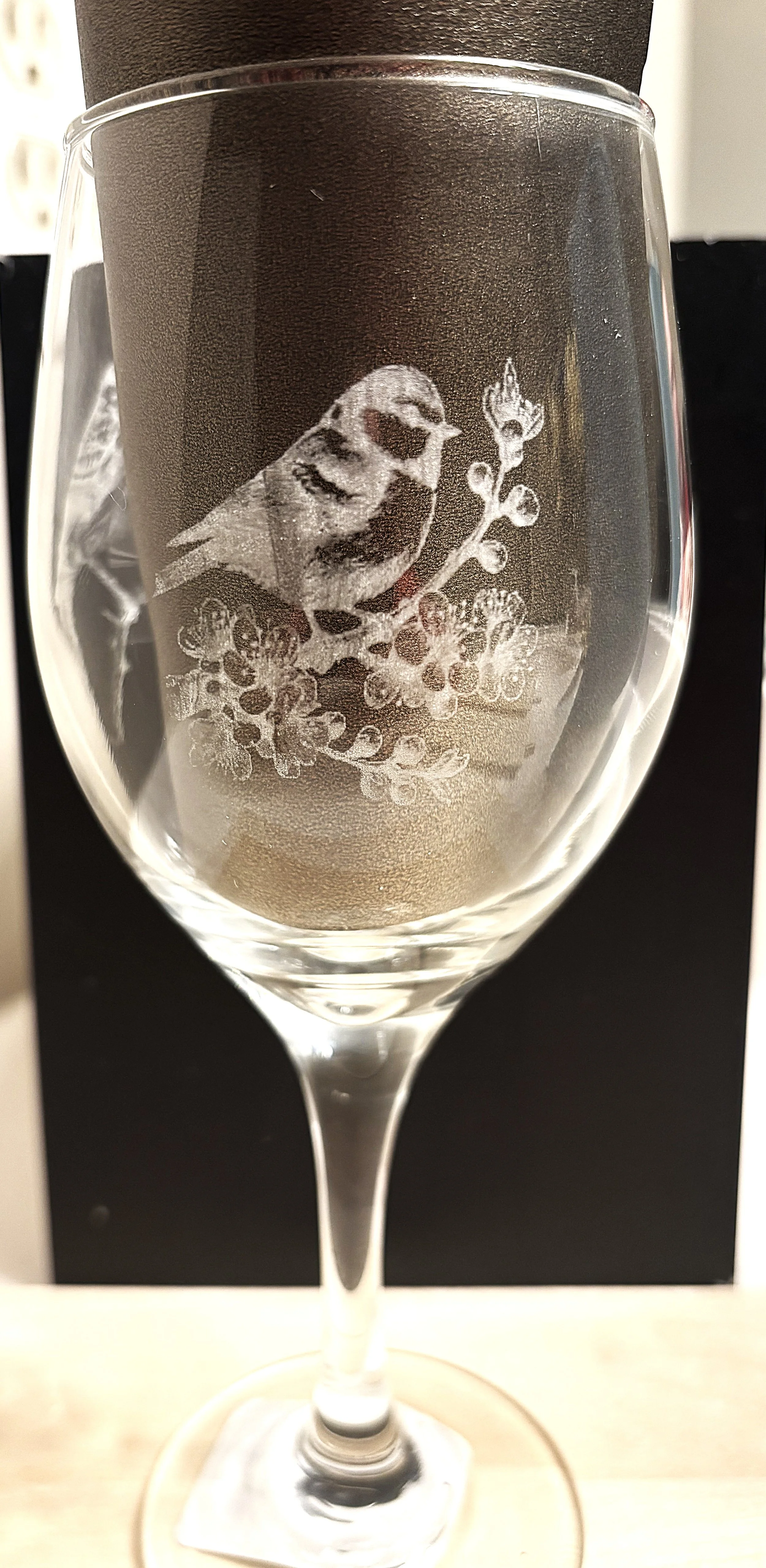 A clear wine glass with etched design of a bird perched on a branch with flowers