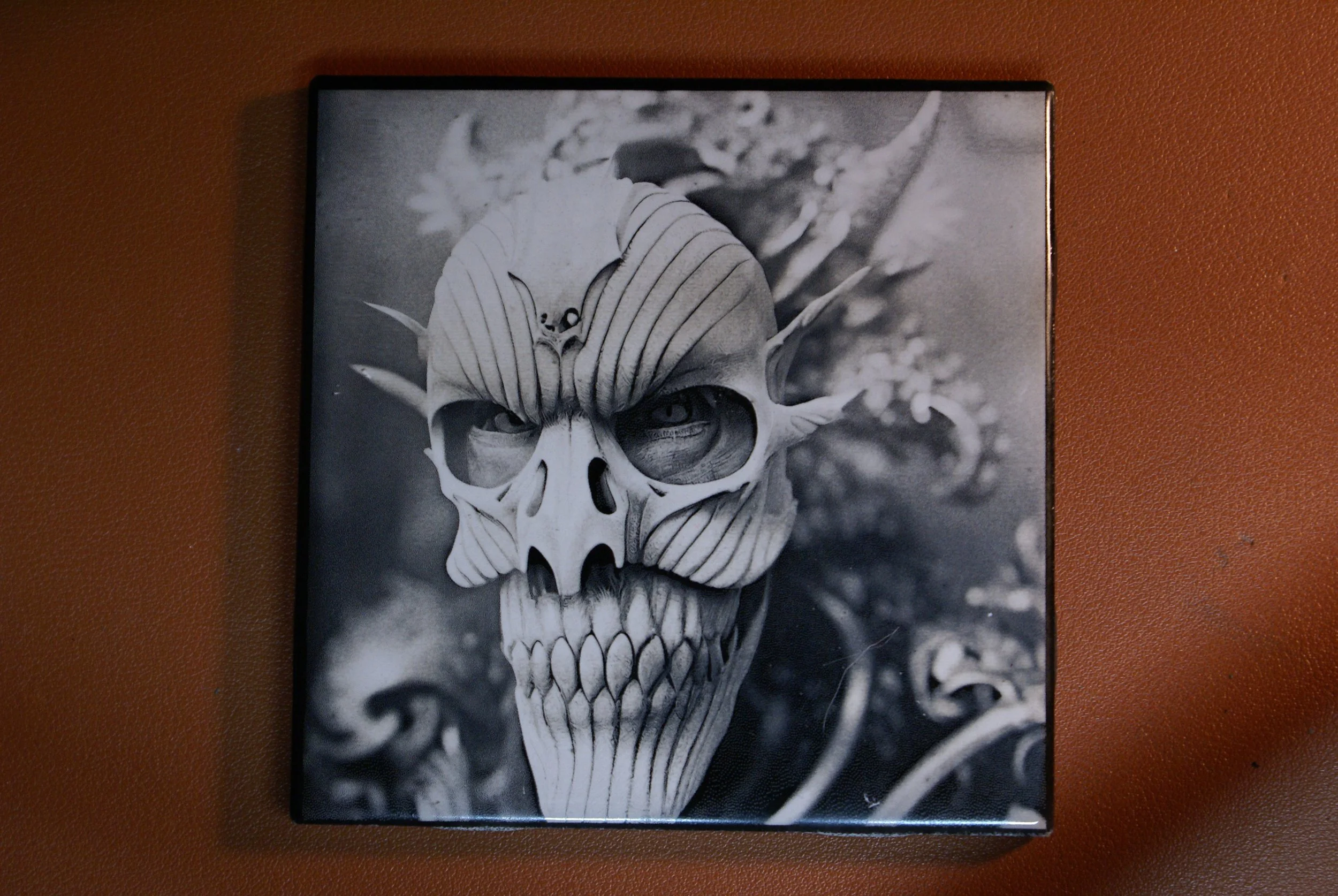 Black-and-white painting of a skull with intricate, striped patterns and pointed bone protrusions on a blurred background, mounted on a wall.