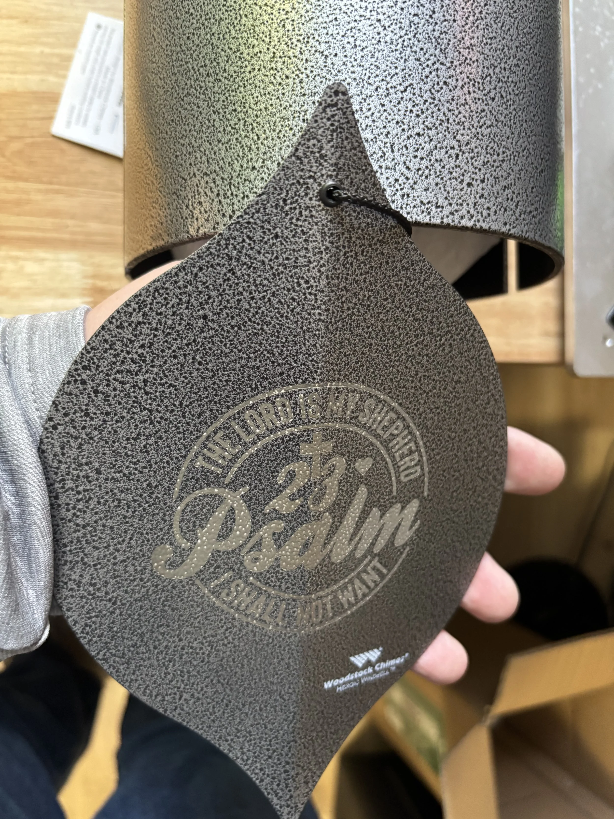 A metallic sign displaying the logo and text for '25th Palm', with the slogan 'The Lord is my Shepherd'. The sign has a textured, speckled finish and is attached with a black cord.