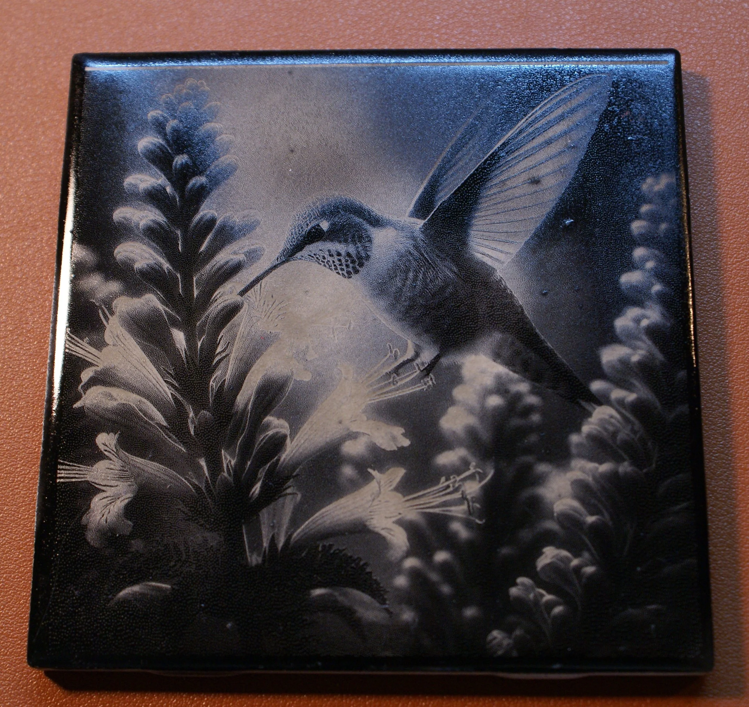 Black and white painting of a hummingbird hovering near flowers.