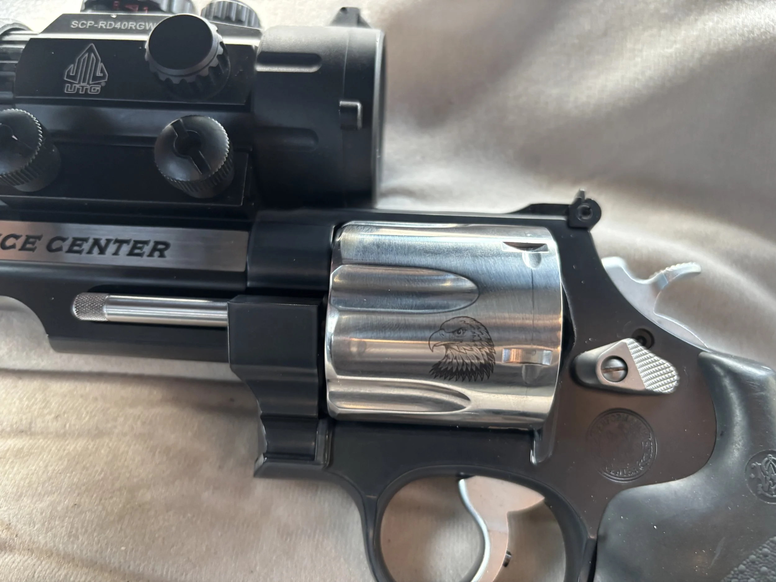 Close-up view of a revolver with a metallic finish and an eagle engraving on the barrel, and a black grip with textured surface.