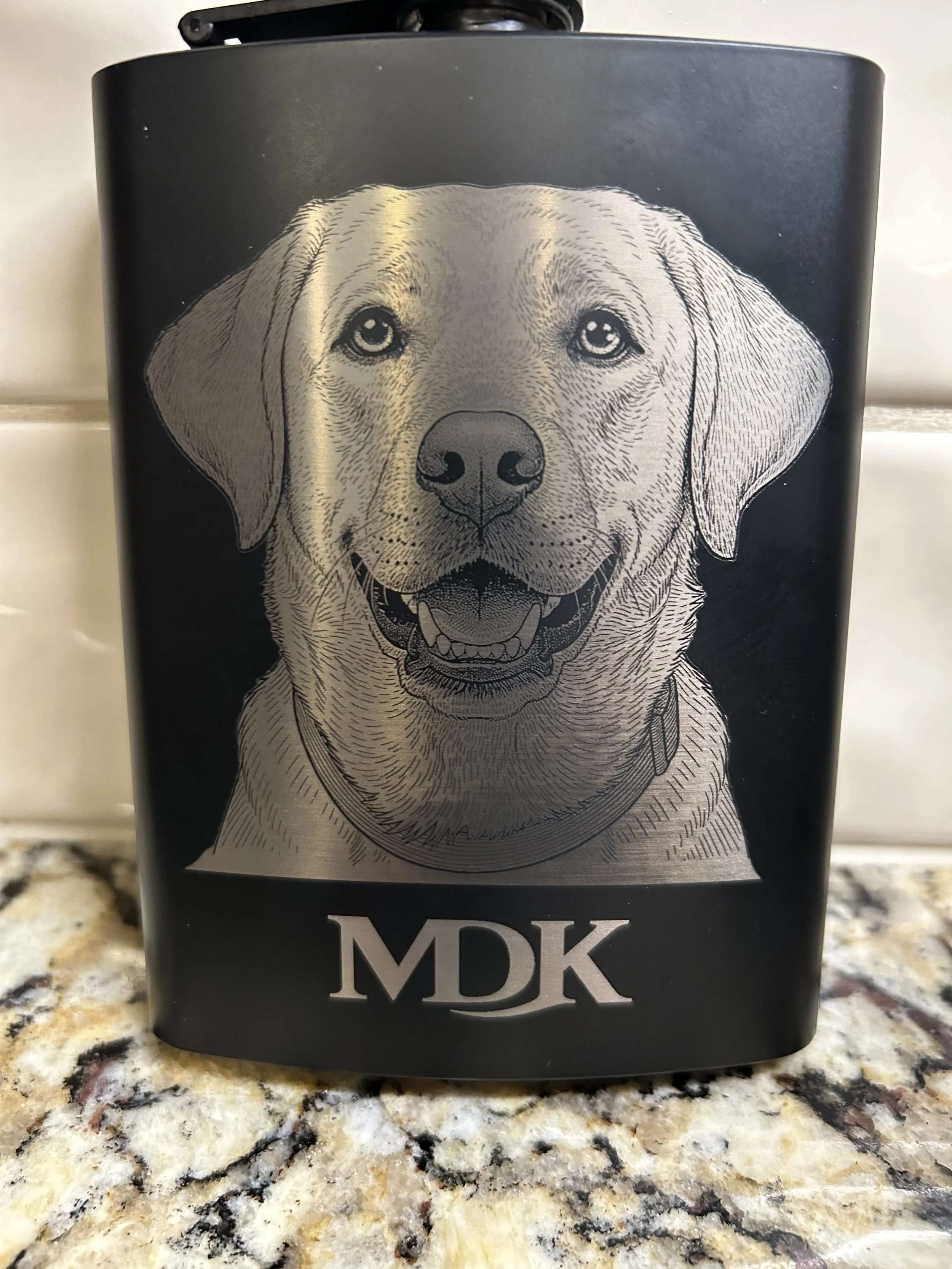 Black container with a detailed illustration of a happy Labrador Retriever dog and the initials 'MDK' at the bottom, placed on a granite countertop.