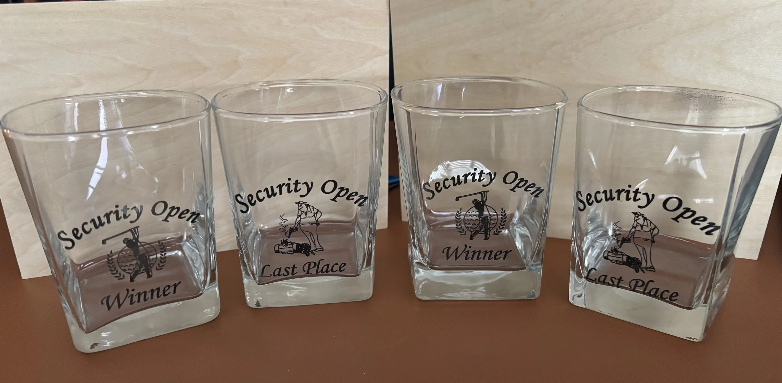 Four clear glass cups with black text and illustrations, labeled 'Security Open Winner' and 'Last Place'.