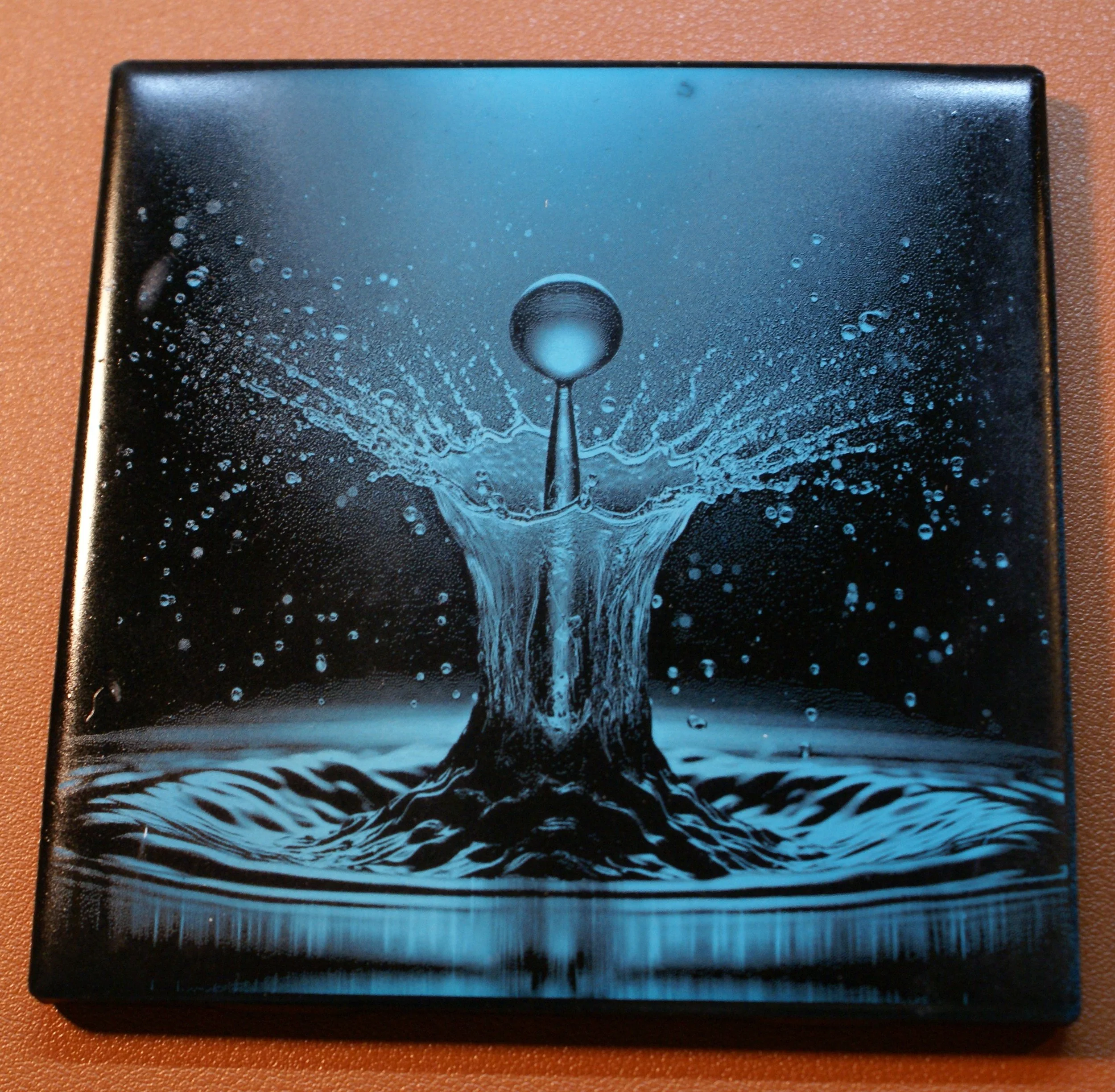 Close-up of a black box with a blue water splash design on the cover showing a water droplet impacting water.