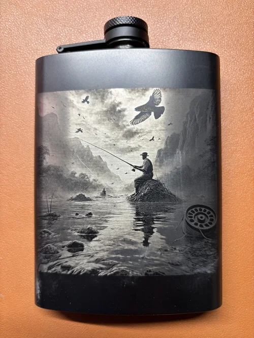 Engraved black flask featuring a fly fisherman in a mountain river.