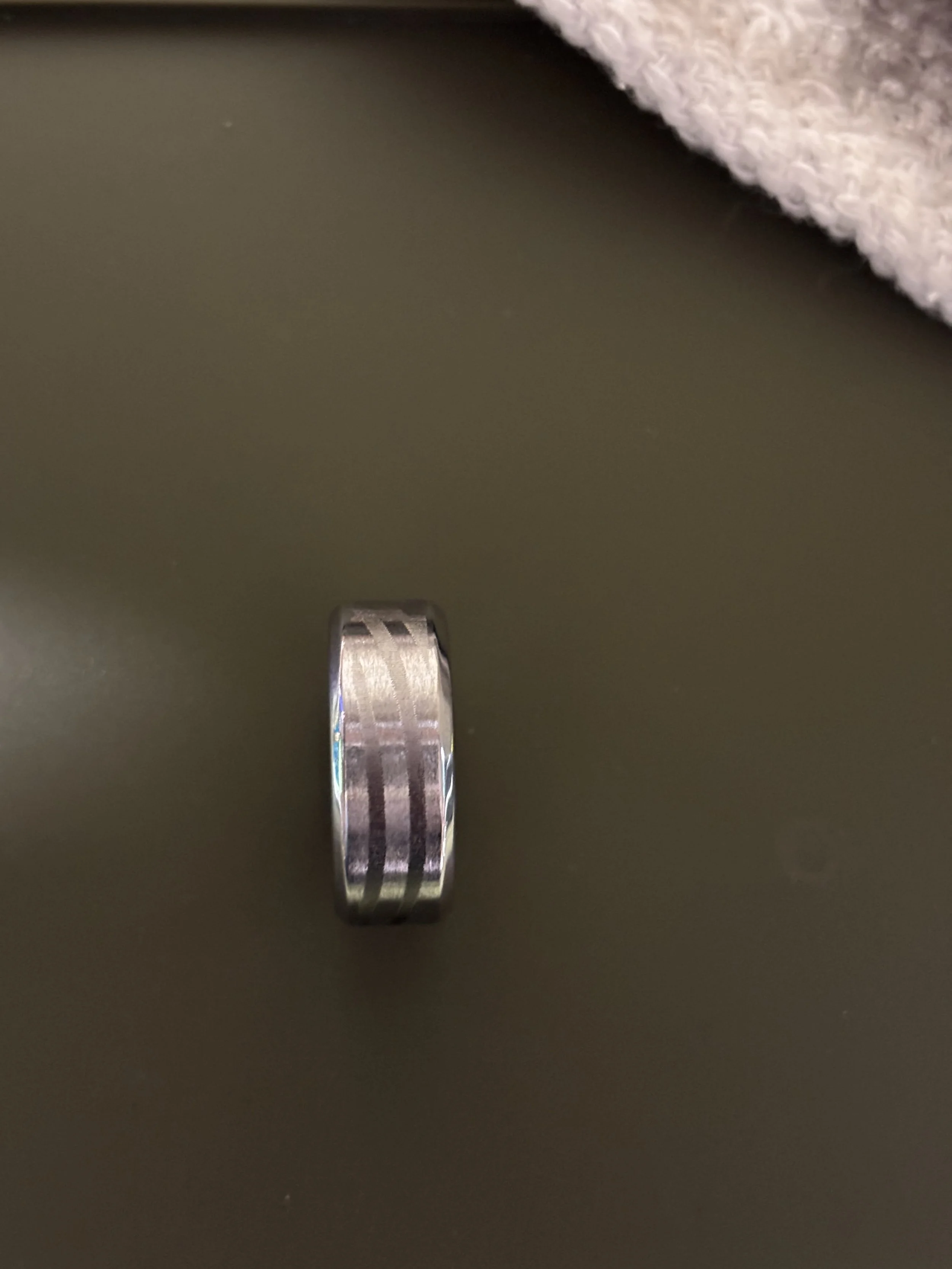 Close-up of a silver ring with engraved patterns on a dark surface, partially covered by a piece of pink and white fabric.