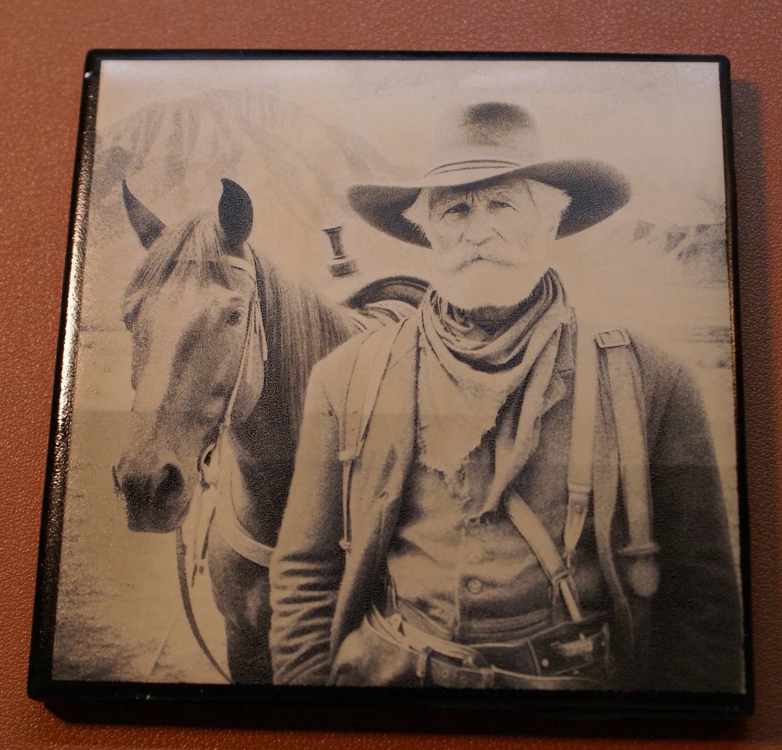 Black and white drawing of an elderly man with a beard in cowboy attire, standing next to a horse, with mountains in the background.