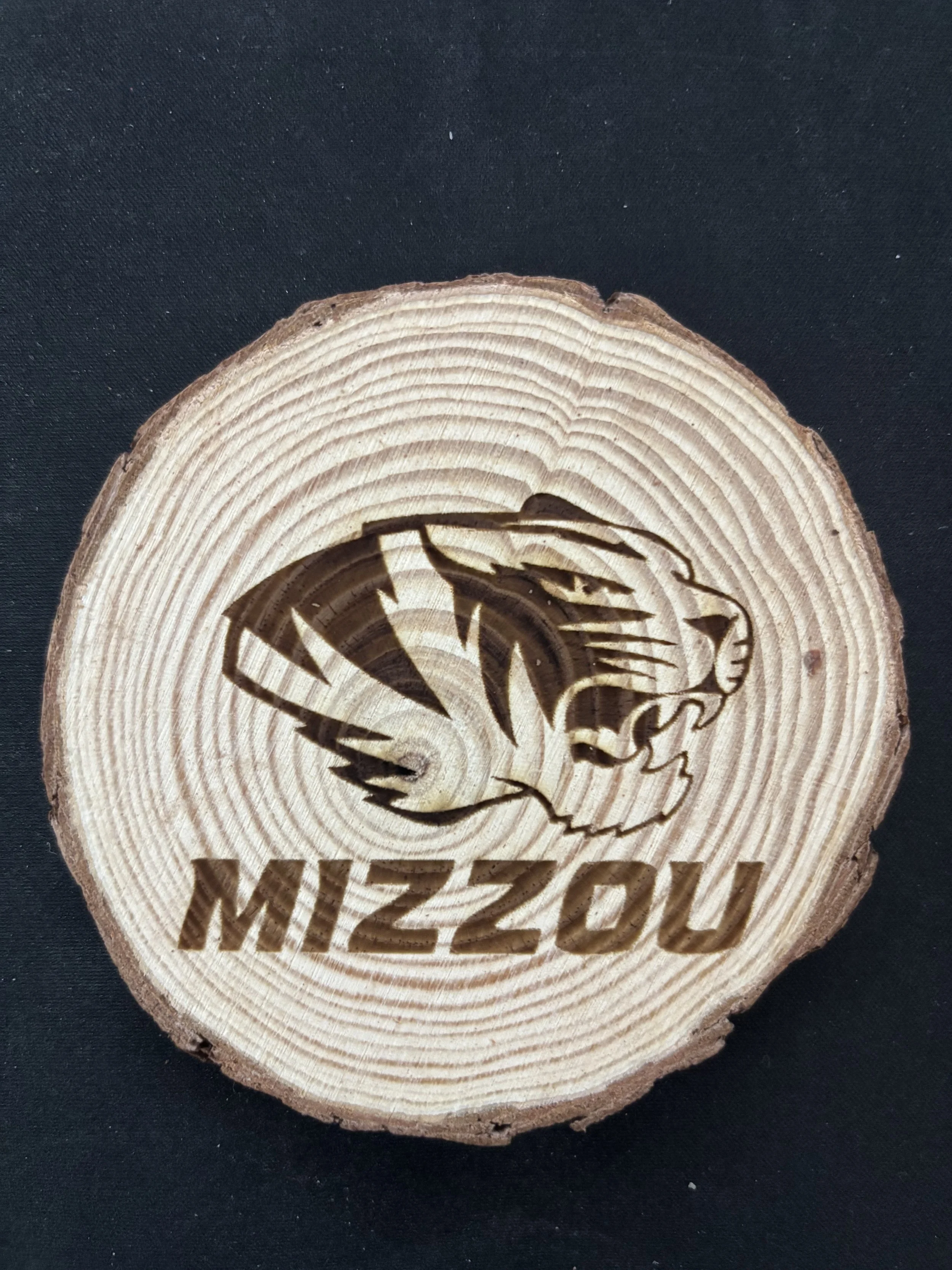 A wooden log slice with a laser-etched logo of a tiger head and the word "MIZZOU" underneath.