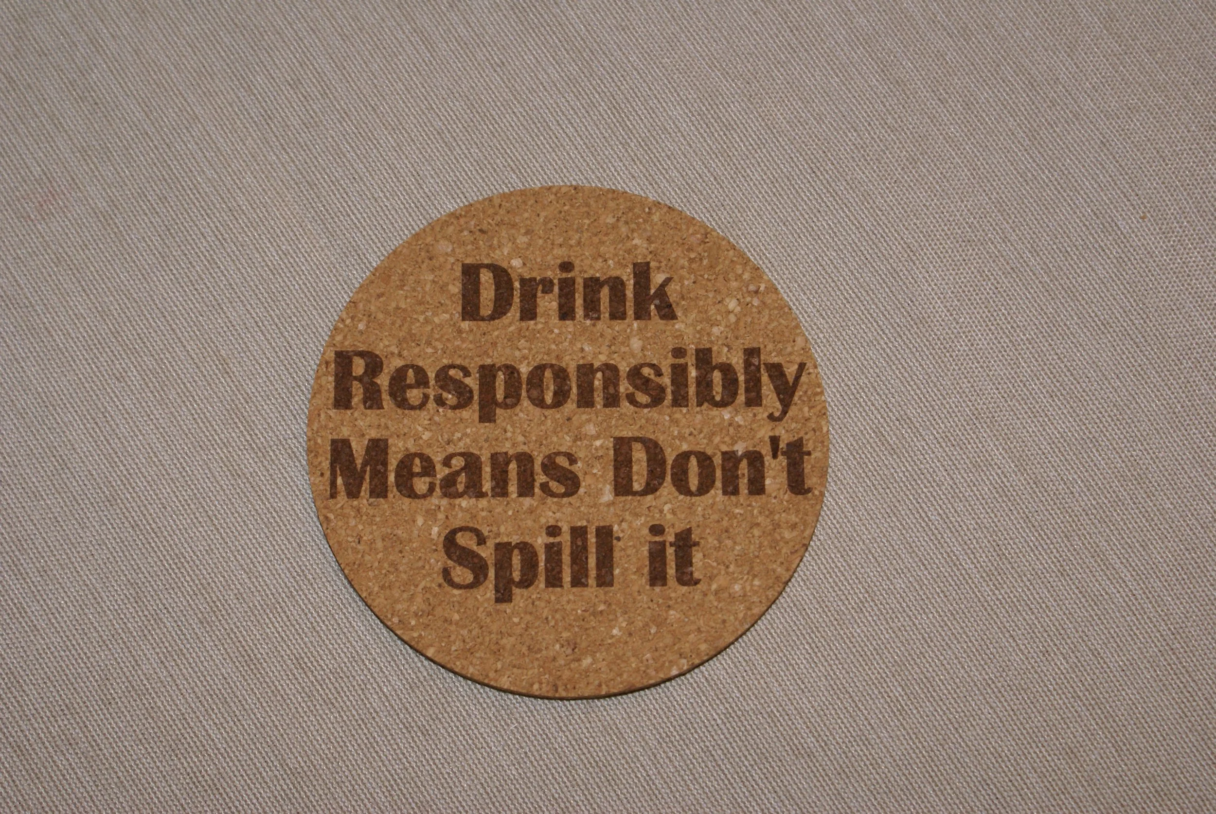 Circular sticker on a surface with the message 'Drink Responsibly Means Don't Spill it' printed in bold brown letters.