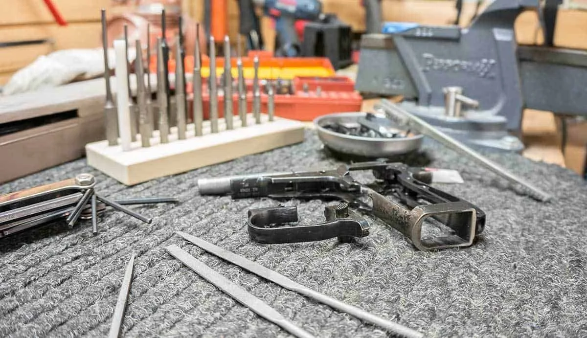 A disassembled firearm on a workbench with tools, bullets, and other gun parts surrounding it in a workshop setting.