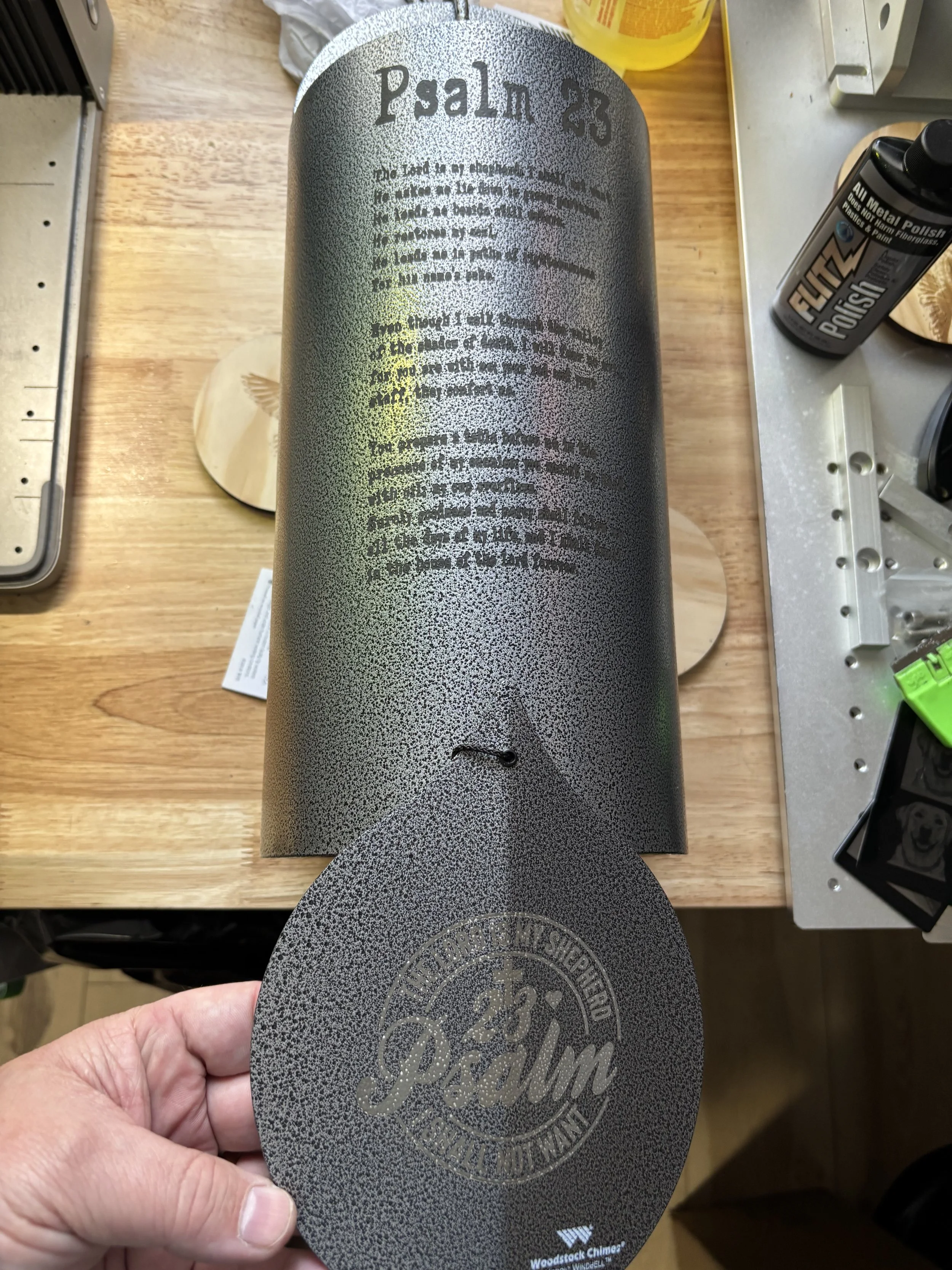 Black spray paint can with gray powder coat finish, labeled Psalm 23, held above a wooden surface, with text and logo on the can.