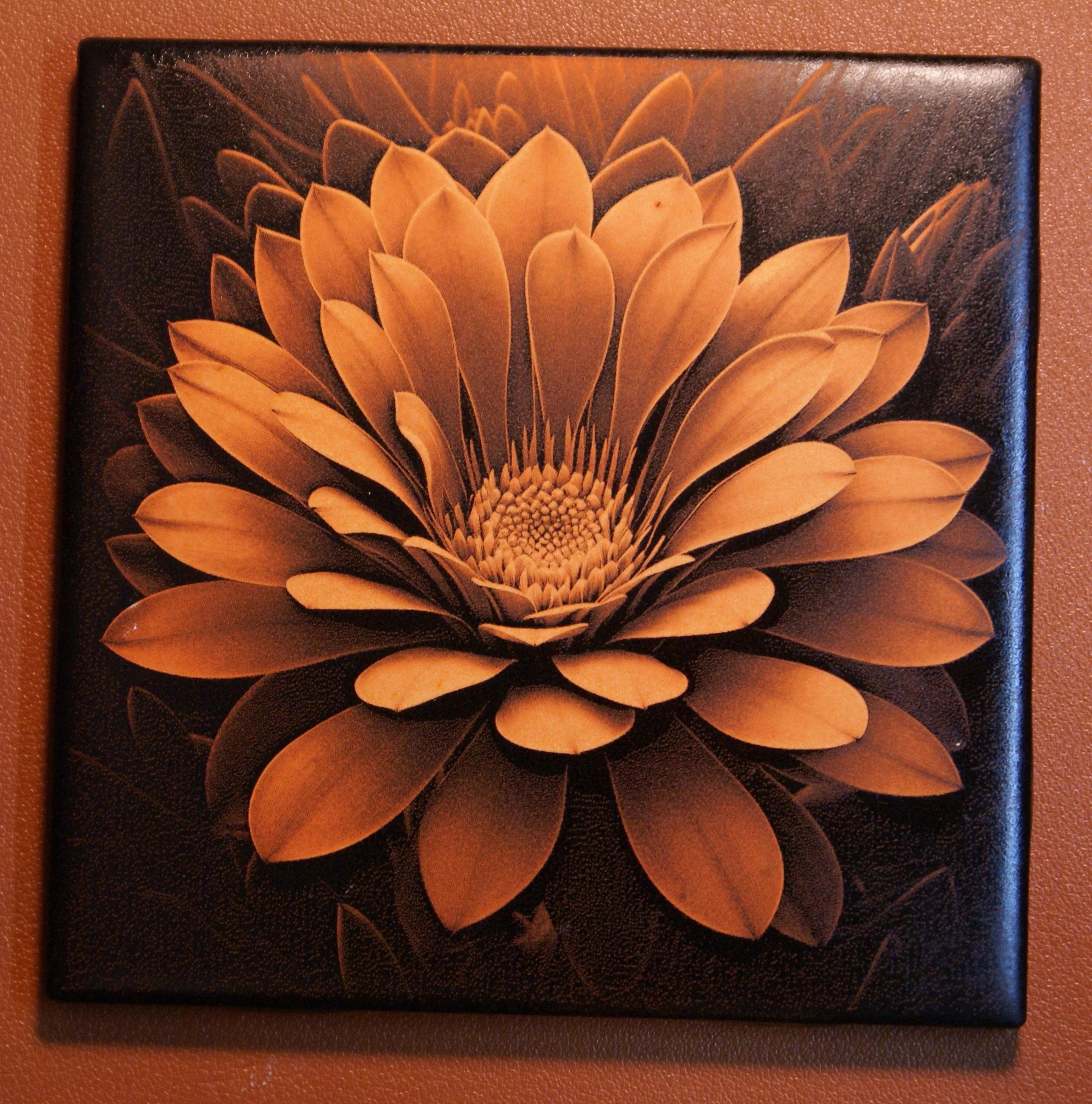 A framed artwork of a large, detailed flower with layered petals, predominantly in shades of brown and beige, on a dark background.