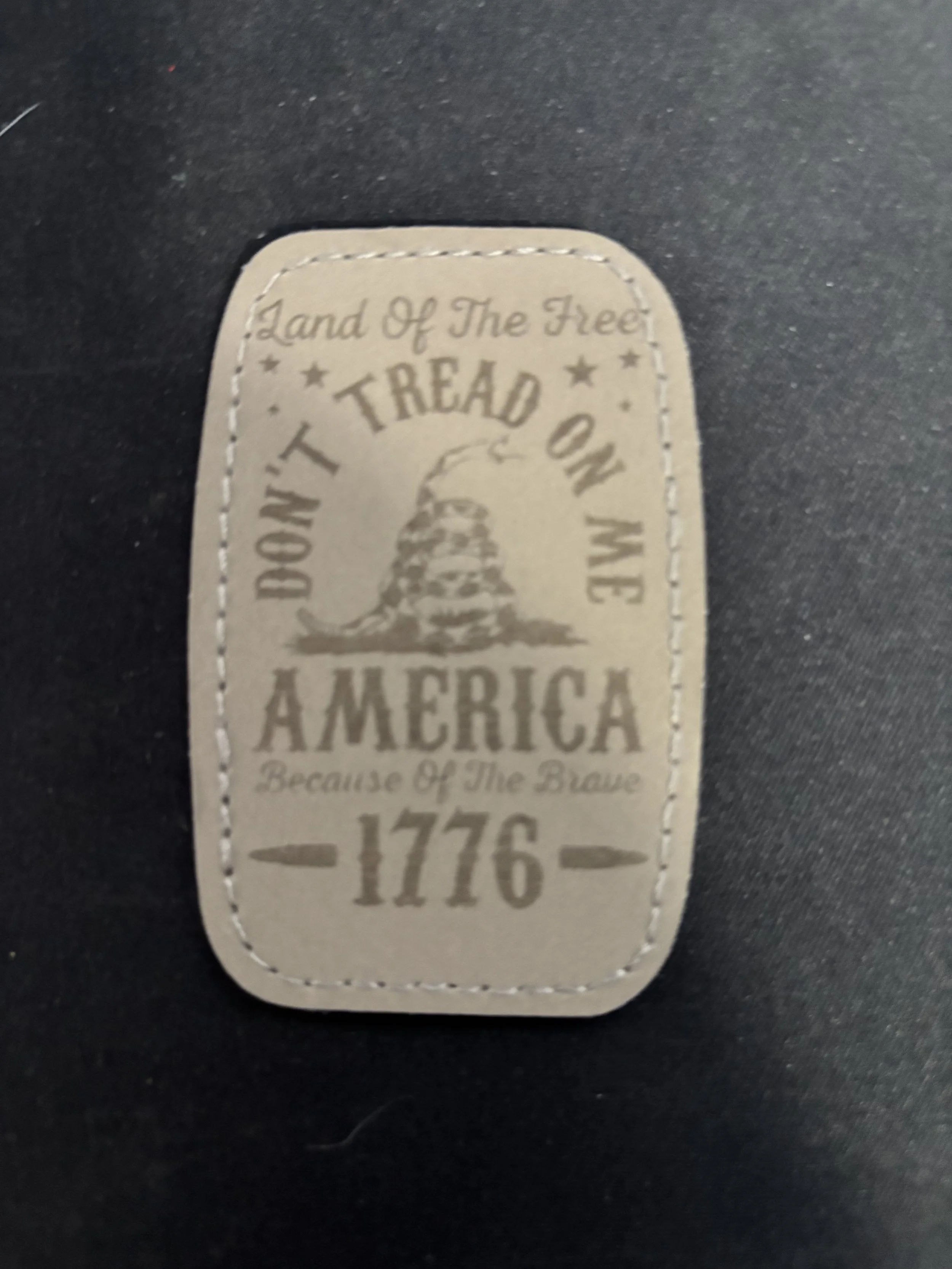 Cloth patch with an American patriotic design, featuring a snake and the text 'Land of the Free, Don't Tread on Me, America, Because of the Brave, 1776'.