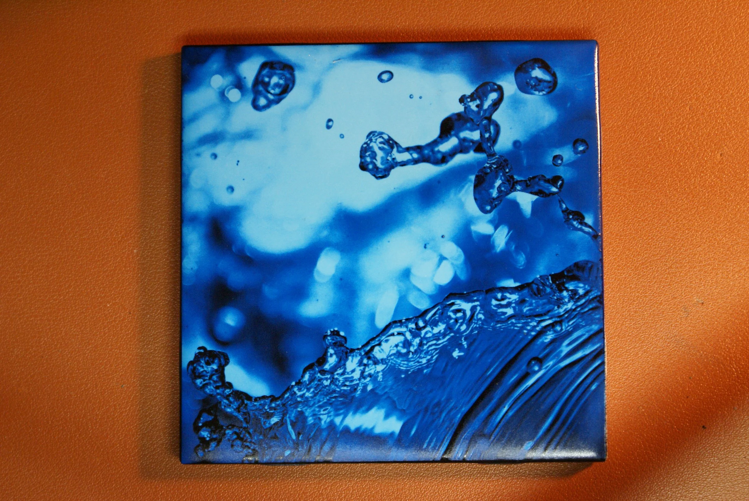 A close-up image of a box with a blue water splash design on its cover, placed on an orange surface.