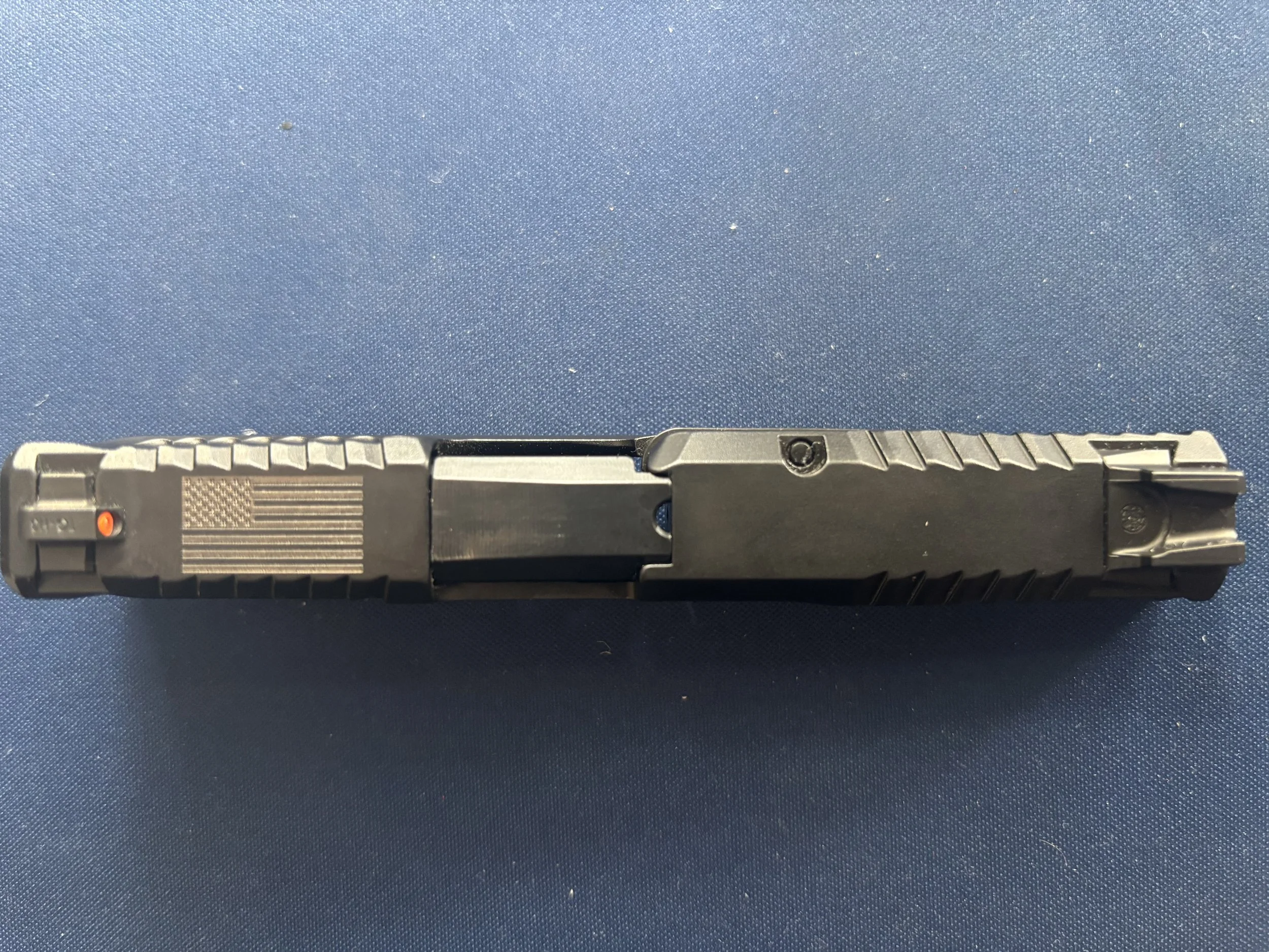 Top view of a black semi-automatic handgun with an American flag engraving on the slide, positioned on a blue surface.