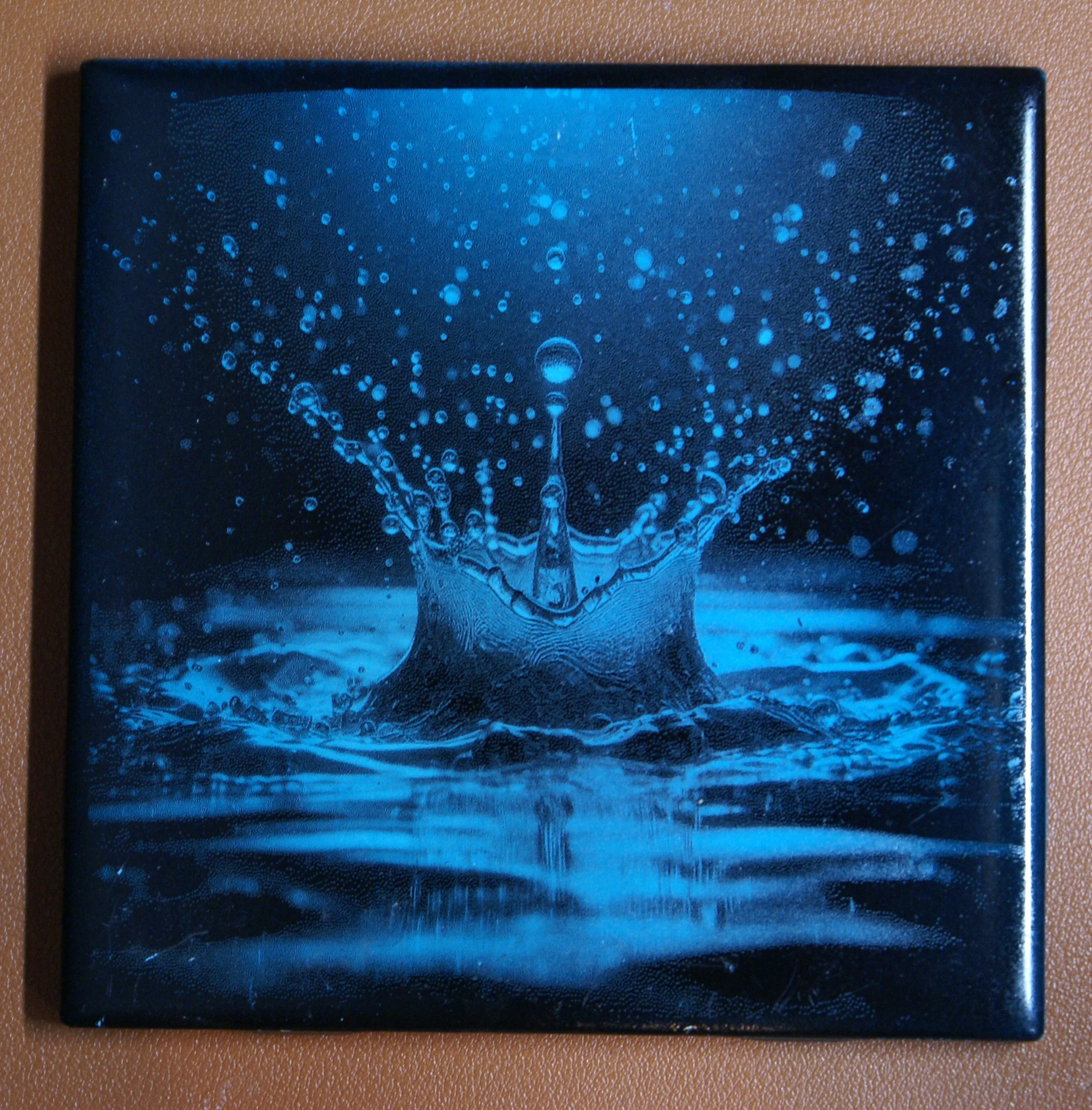 Blue-tinted photo of a water droplet splash with water droplets scattering outward.