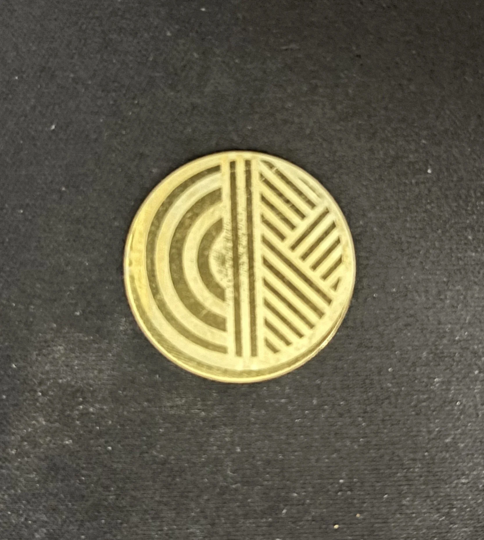 Close-up of a round gold-colored coin with geometric patterns on a black surface.
