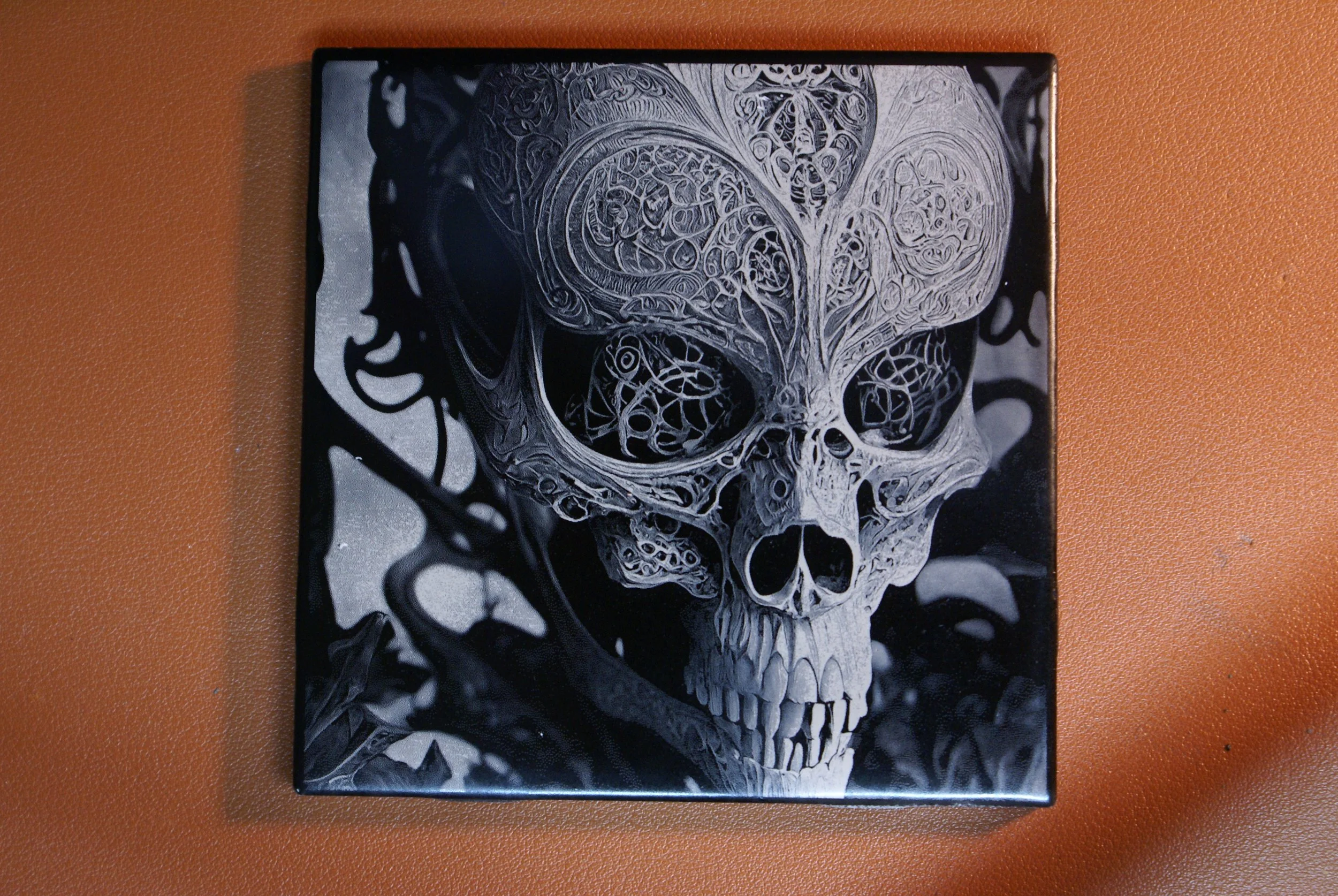 Black and white artwork of a detailed skull with intricate, swirling patterns, set against a dark background.