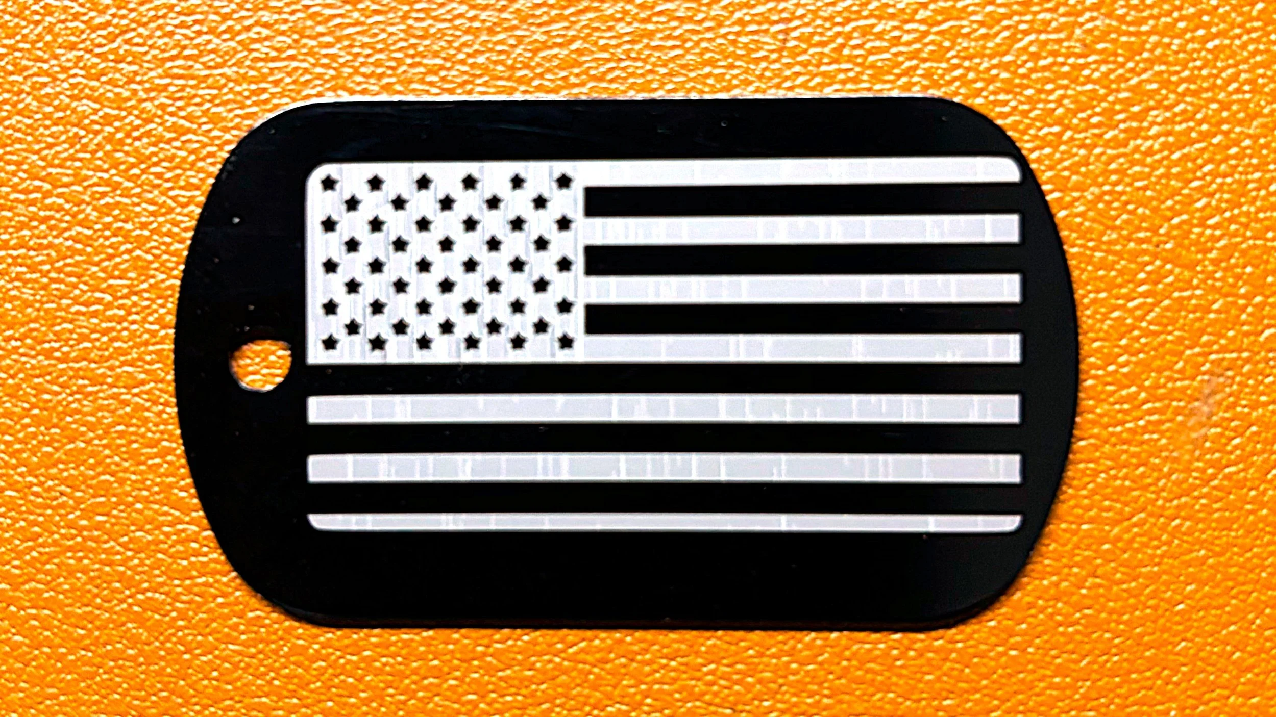 A black metal tag with an American flag design cut out, placed on an orange textured surface.