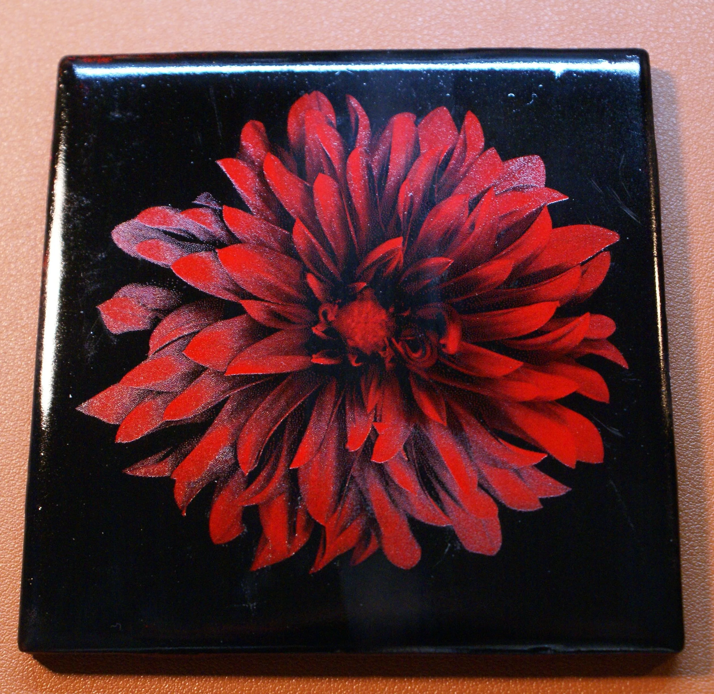 Black square box with a large red and black flower design on top.