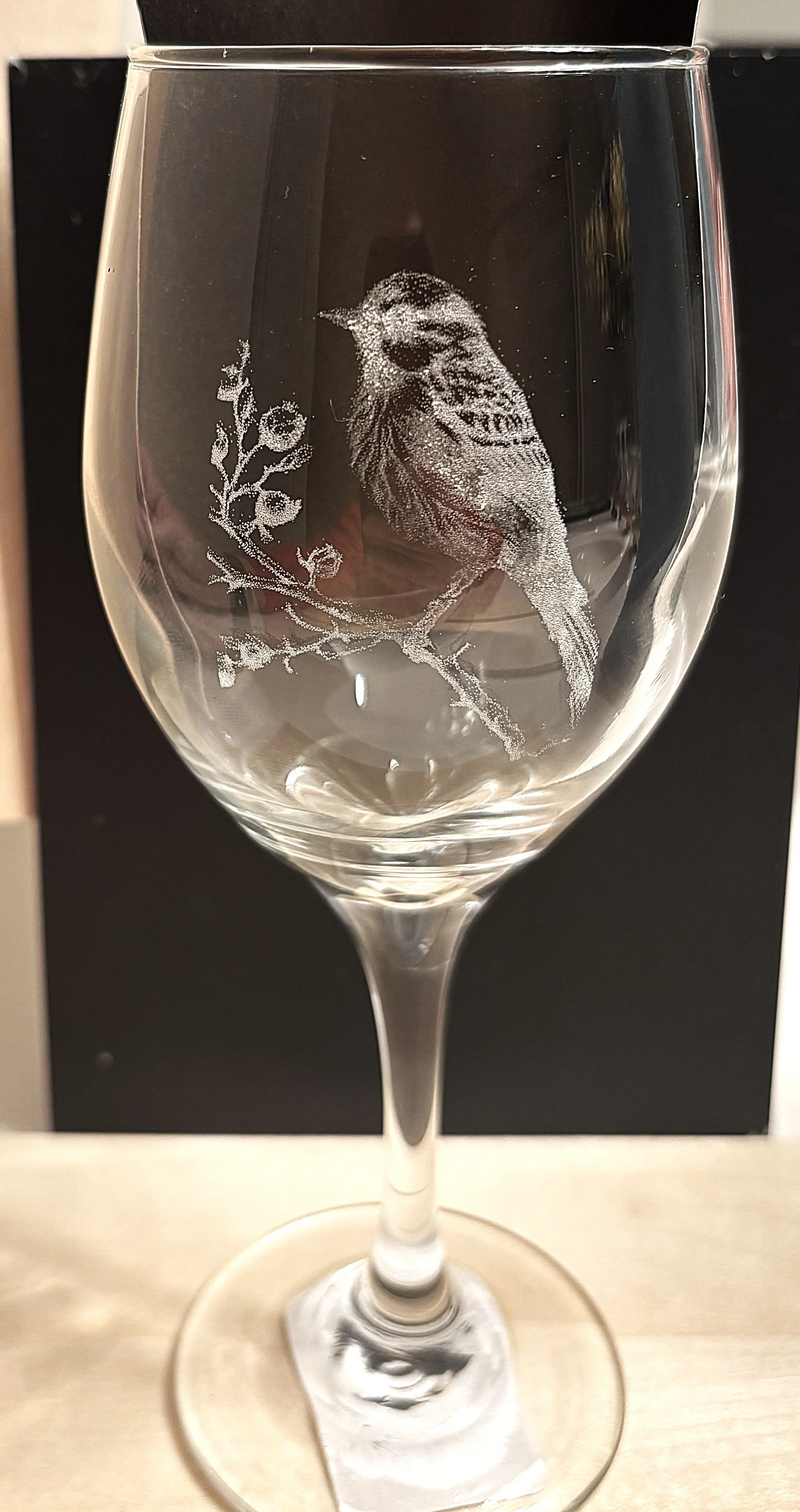 A clear wine glass with an etched design of a bird perched on a branch with flowers.